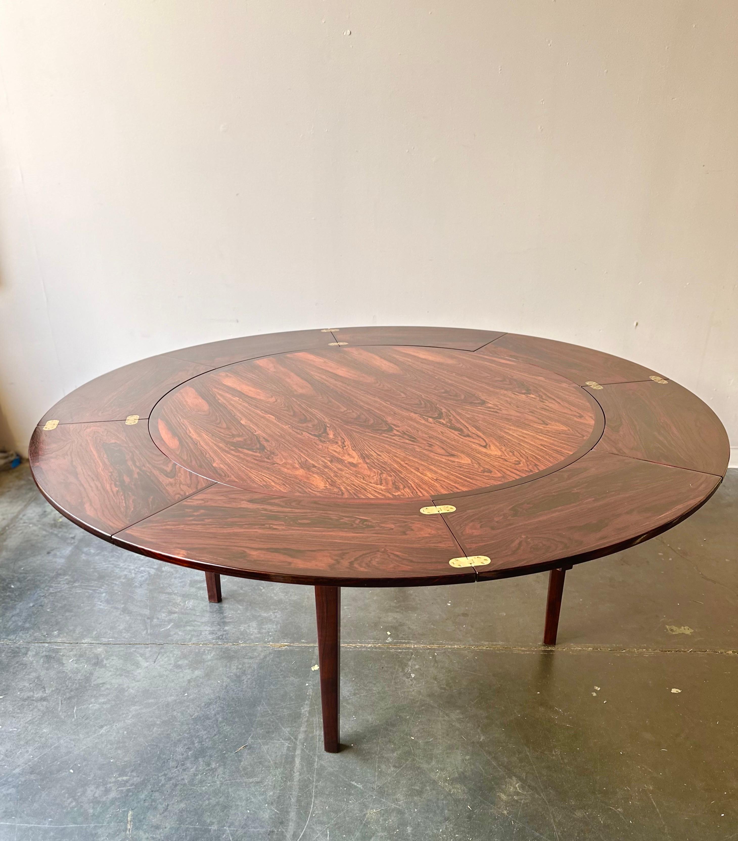 The Dyrlund Flip Flap Lotus Dining Table is a remarkable piece of mid-century modern furniture, designed and crafted in Denmark in the 1960s. This unique dining table features a round rosewood top supported by four tapered legs, embodying the