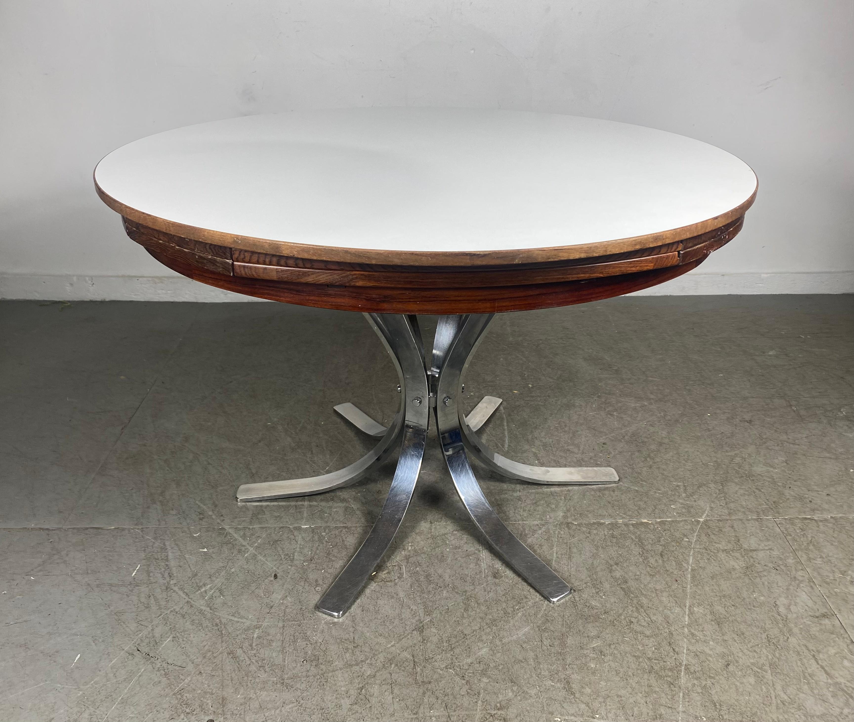 Seldom seen Rosewood and Laminate dining table by Dyrlund circa 1960s Denmark. The table features a round top situated on a six legged chrome pedestal base. This table expands by opening up like a lotus flower. The otter edges of the table fold out