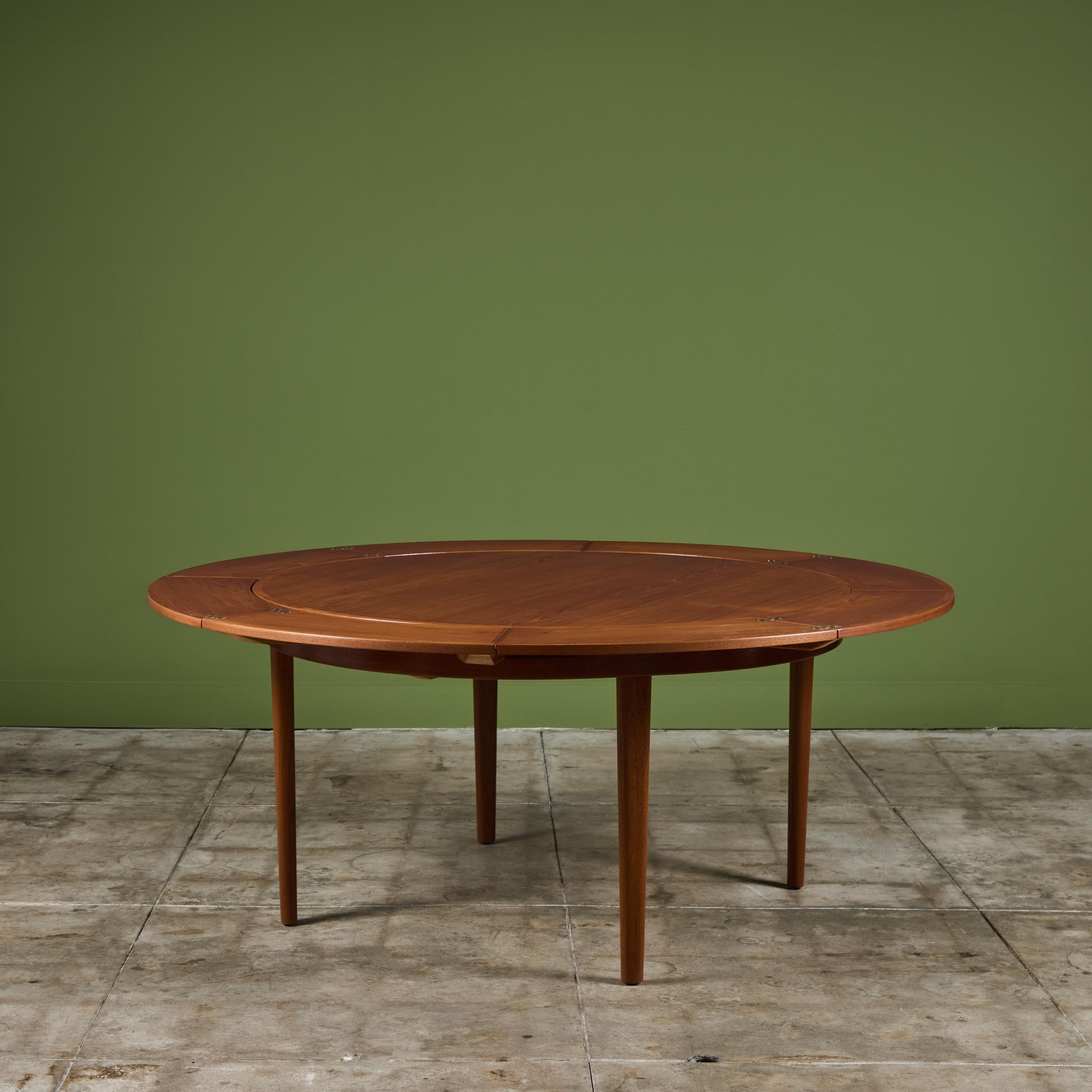 Teak dining table by Dyrlund, c.1960s, Denmark. The table features a round top situated on four tapered legs. This table expands by opening up like a lotus flower. The outer edges of the table fold out and open in a 'flip flap
