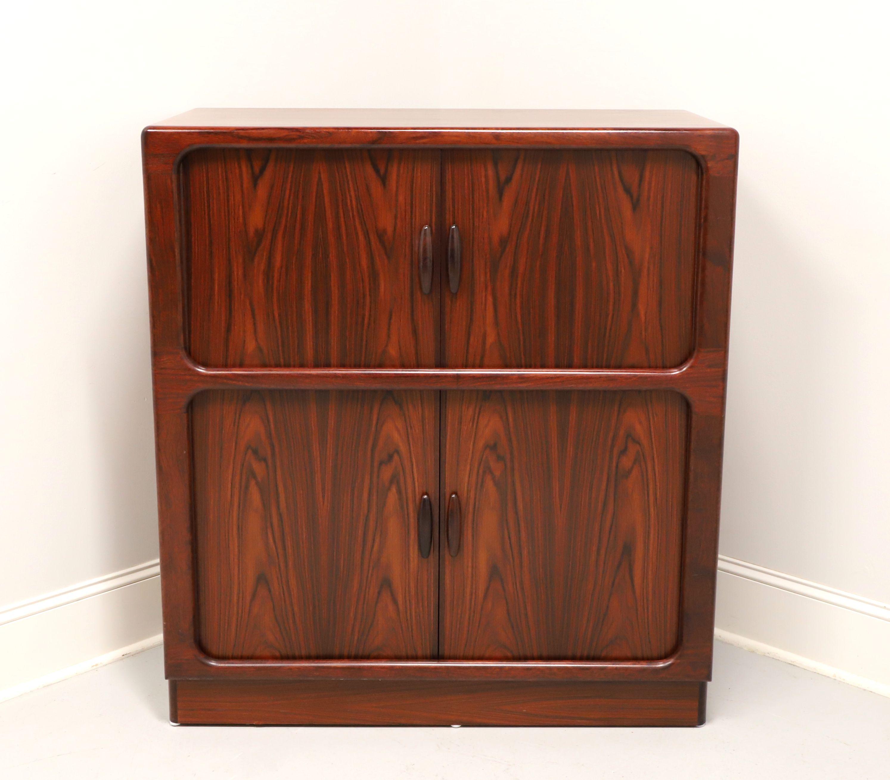 A Danish Modern style bar cabinet by Drylund. Rosewood, retractable tambour doors and rosewood handles. Features upper lighted cabinet with two retractable doors revealing a mirror back, one fixed wood shelf and a pull-out laminate top surface.