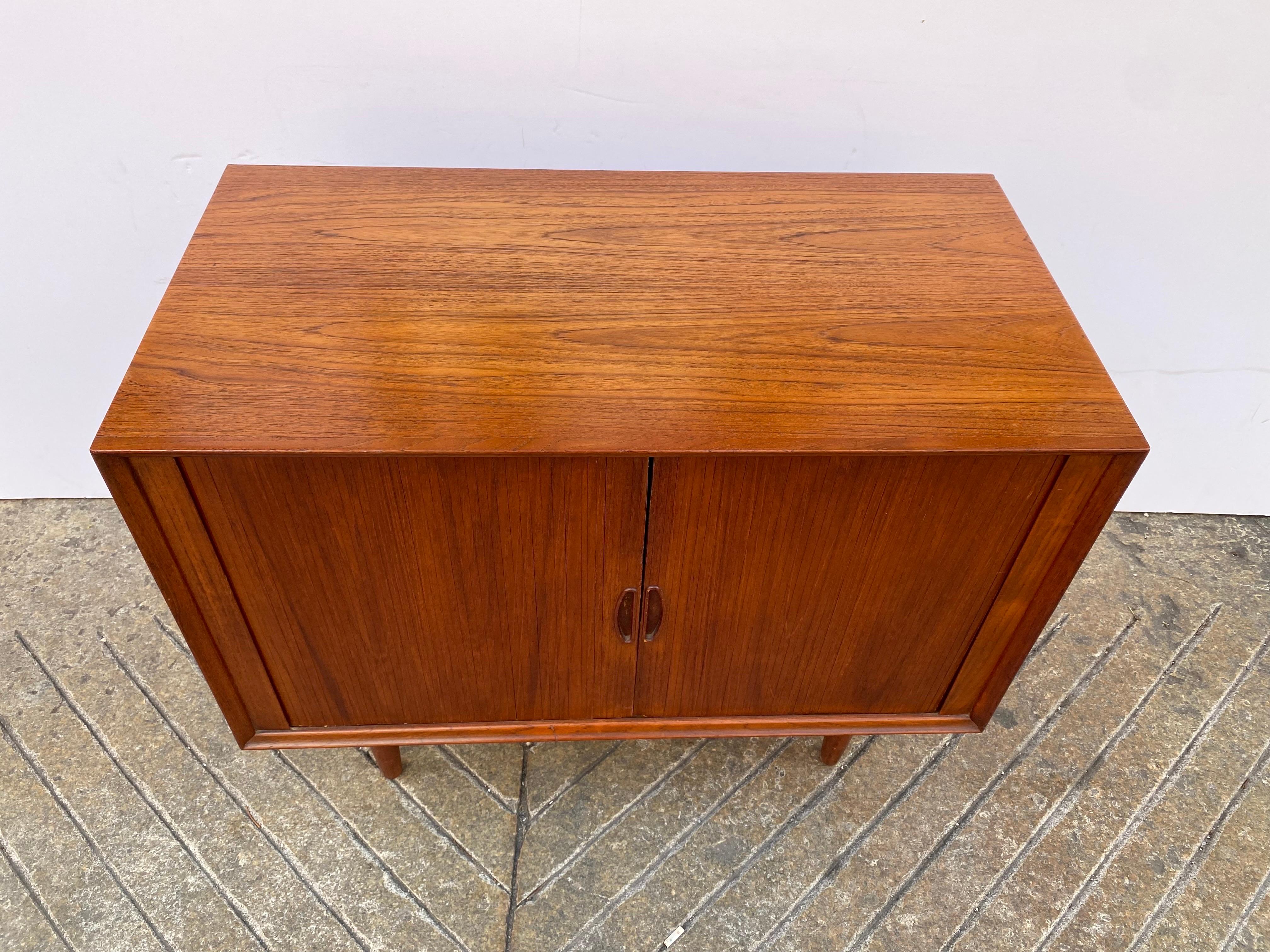 Dyrlund teak tambour door cabinet. Doors slide open to reveal an adjustable shelf. Useful and Beautiful Design! Top has been refinished. Typical signs of use and wear, but overall looks very good!