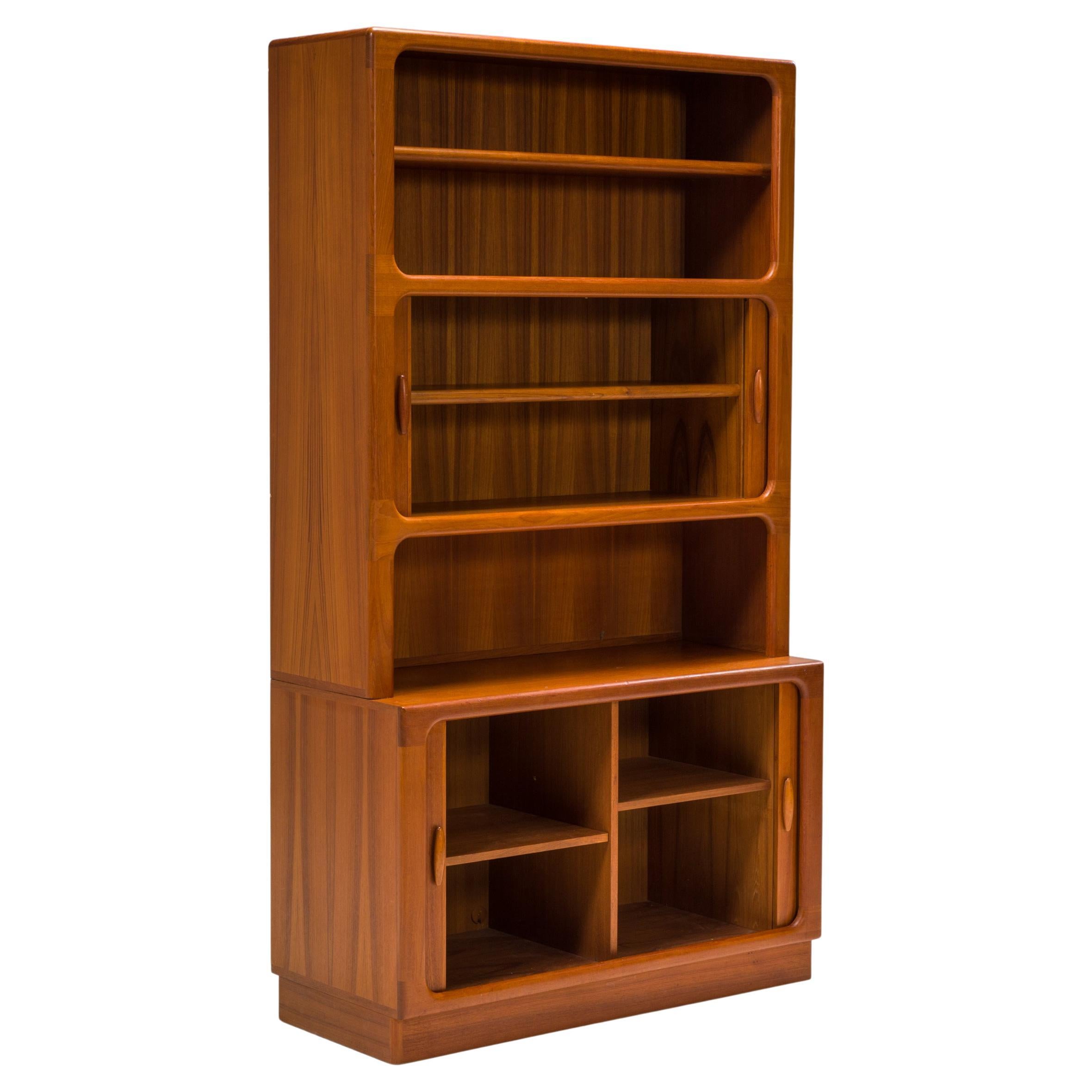 Designed and made in Denmark by Dyrlund, this cabinet is constructed from solid teak wood.

The bookshelf features a large base cupboard with two compartments, each with a shelf and closing with two tambour sliding doors.

A narrower cabinet sits on