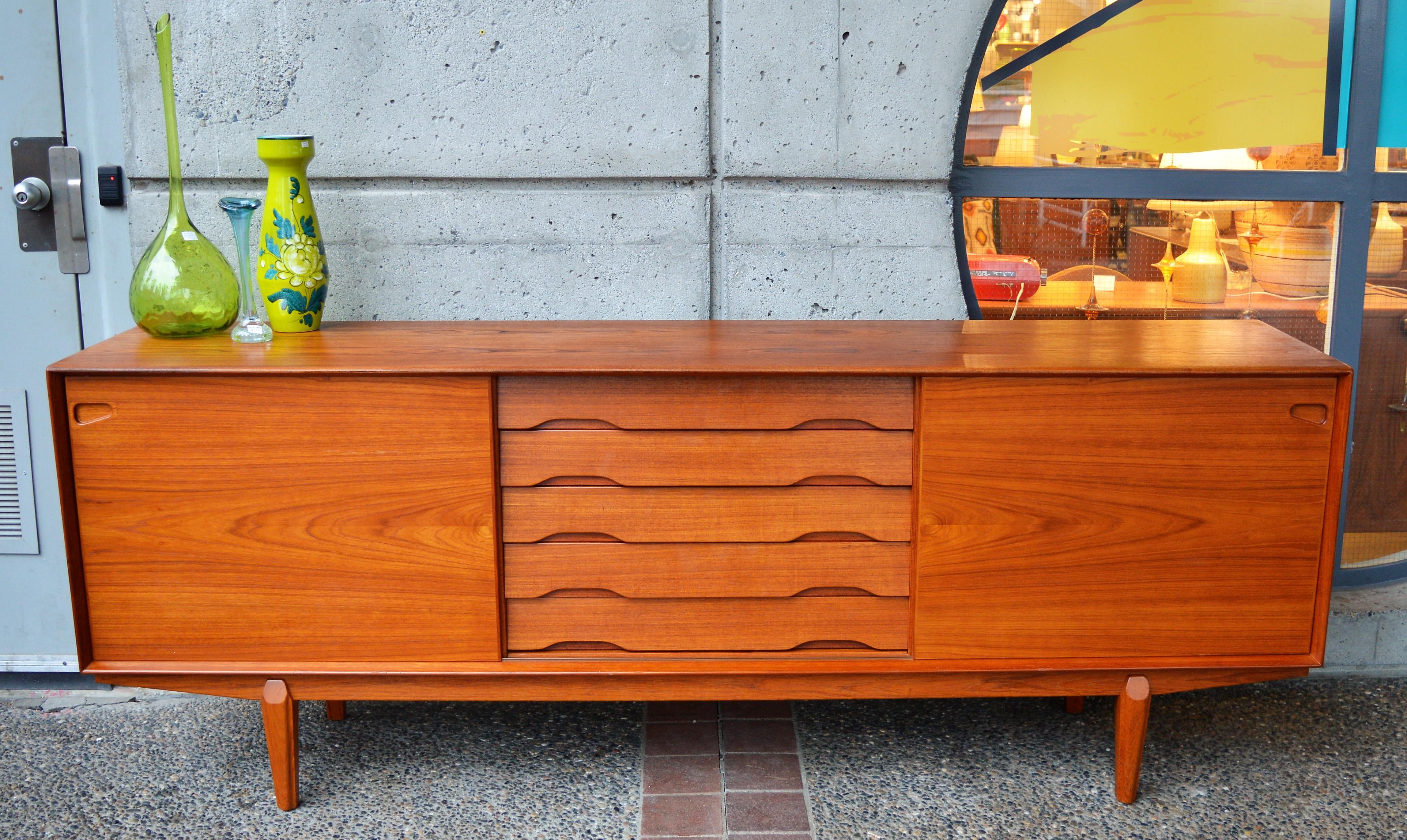 This spectacular quality Danish modern teak credenza or sideboard was designed in the 1960s by Rosengren Hansen for Dyrlund. Featuring center louvered drawers with fun double cut-away handles and wood drawer frame construction with dovetail joints,