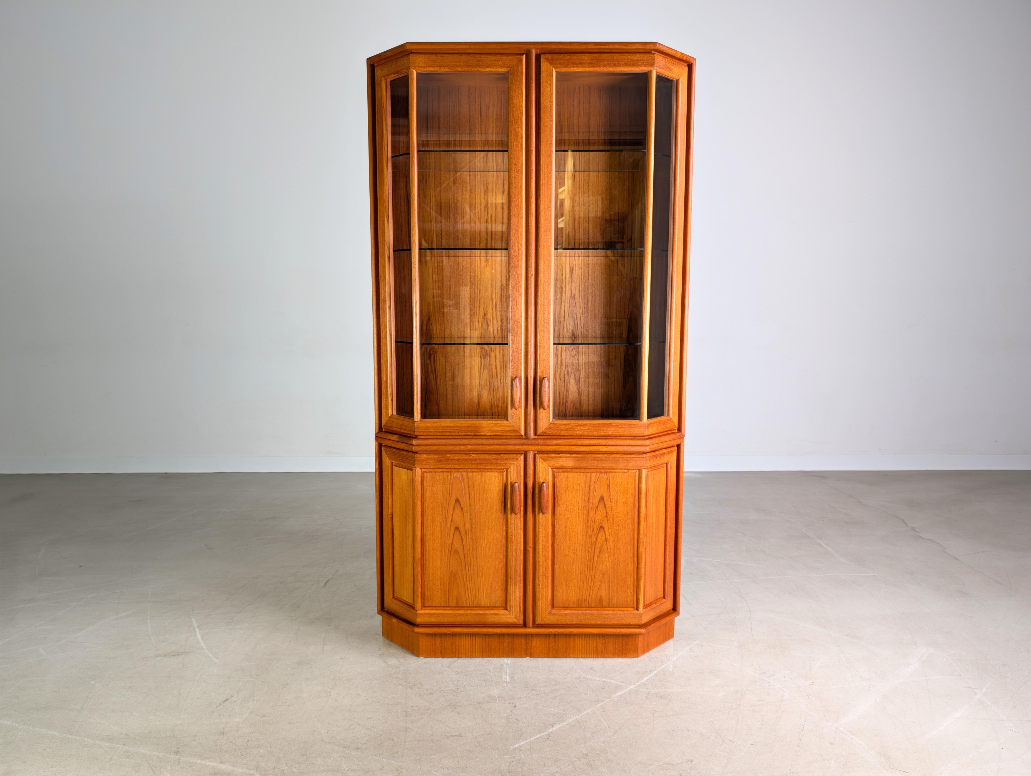 Wir bieten eine wunderschöne Vintage Teak Vitrine vom dänischen Traditionshersteller Dyrlund zum Verkauf an. Das Möbel verfügt über zwei Holztüren im unteren und zwei verglaste Türen im oberen Bereich, hinter denen sich ein höhenverstellbarer Holz-