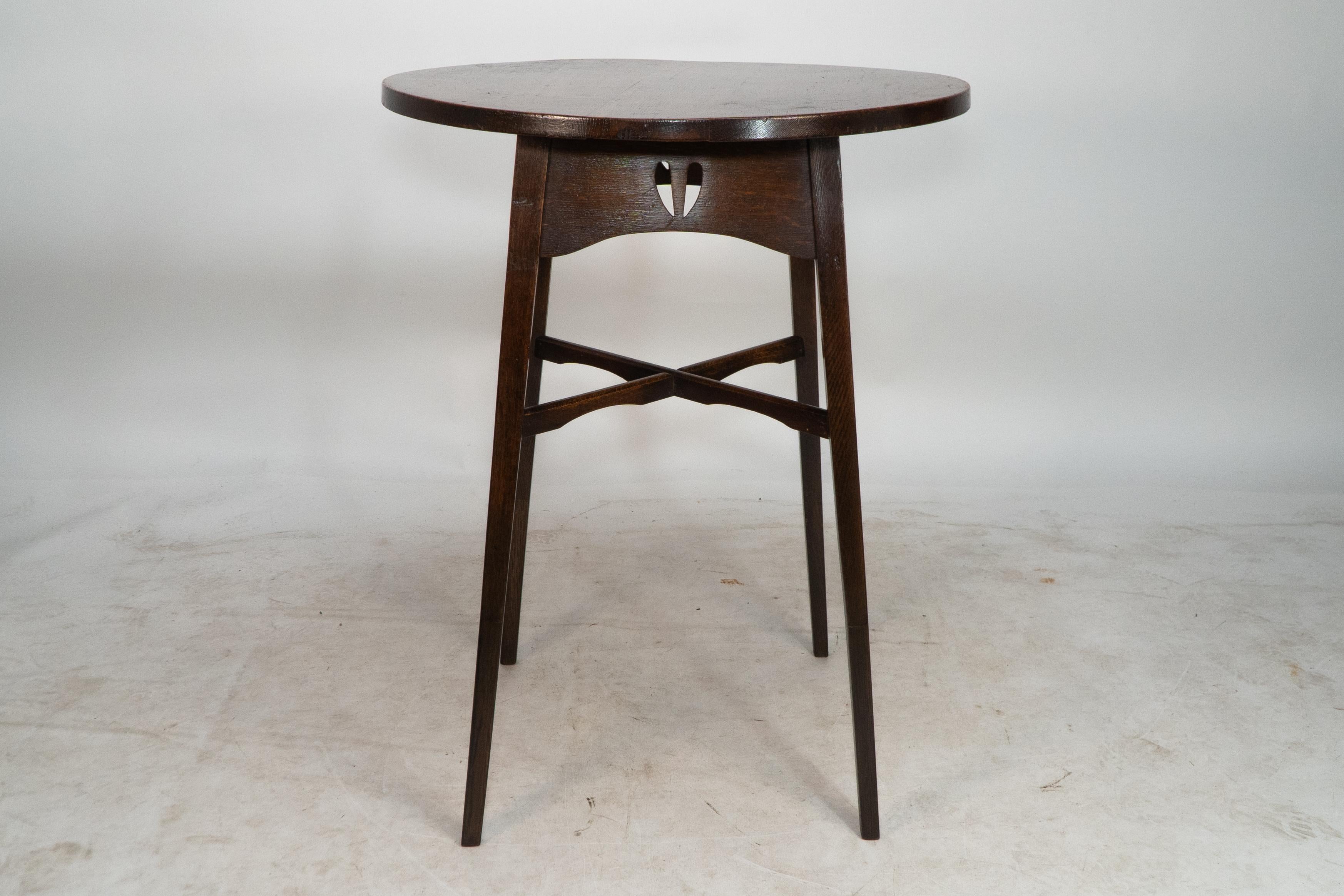 E A Taylor for Wylie and Lochhead. A Glasgow school circular oak side table with shaped skirt and twin heart through cut-outs. The square tapering legs are united by a fine cross stretcher with subtle shaped decoration.
