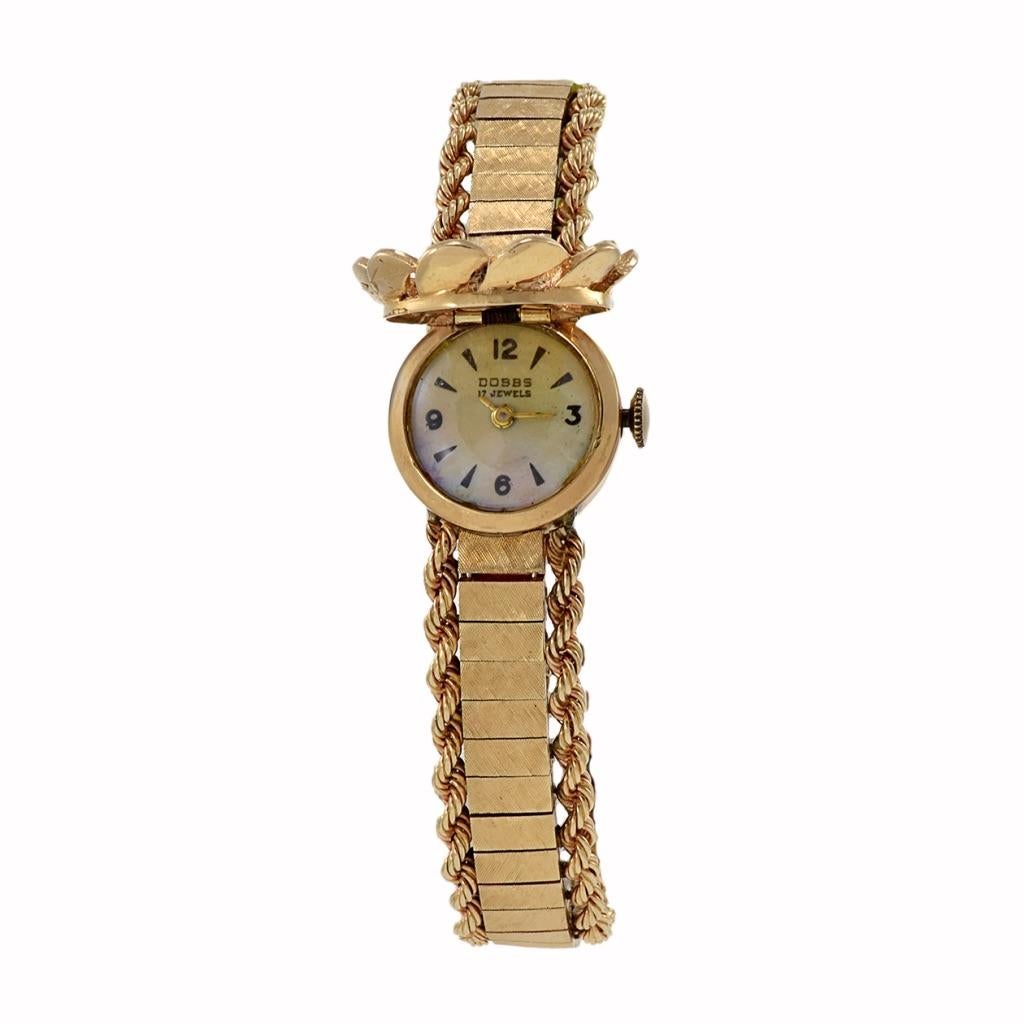 The Dobbs timepiece from the 1960s showcases a stunning design with its 14Kt yellow gold case and double rope 14K gold bracelet, epitomizing vintage elegance. Its unique feature includes a flower-shaped flip top adorned with diamonds totaling 0.25