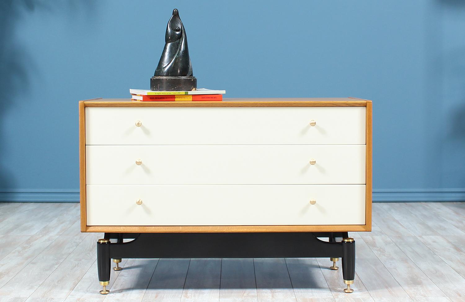 Elegant chest designed by E. Gomme for G-Plan in the United Kingdom circa 1960’s. This beautiful three-drawer chest is crafted in oak wood with complimenting white lacquered drawer fronts and sits on an ebonized wood base with brass feet that match