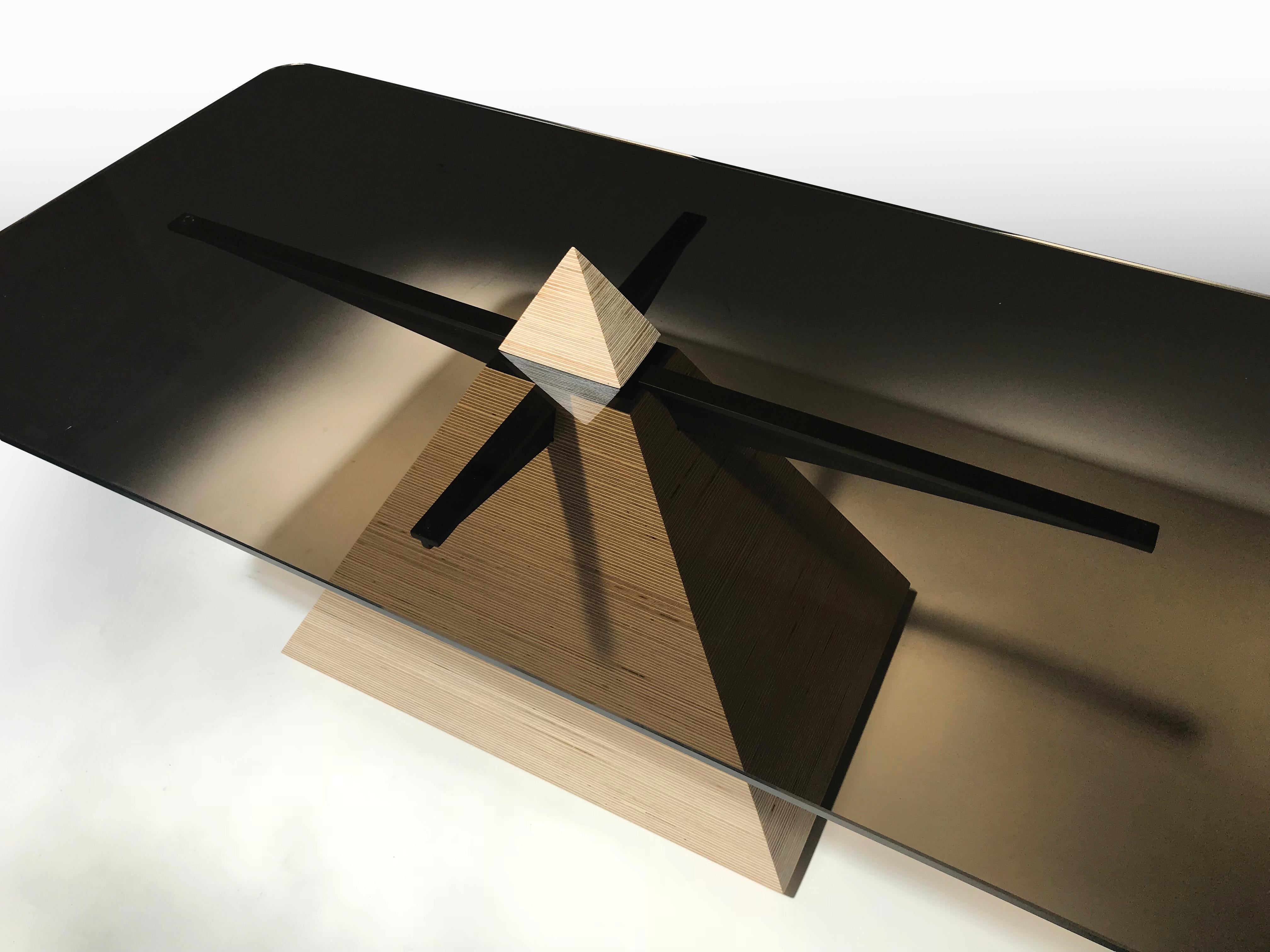 EÆ Pyramid Halo table in laminated Finland Birch plywood and black glass. An exercise in intersecting geometry and materials. The pyramid base appears to pierce through the smoked glass top while a blackened steel armature supports the table top