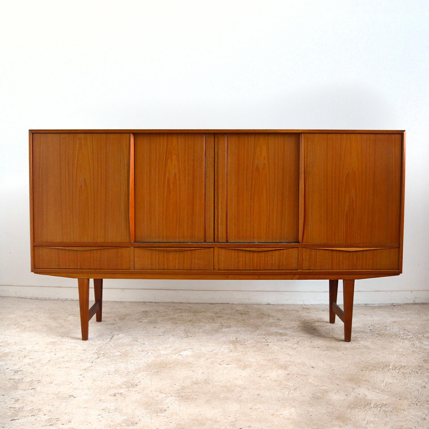 This stately E. W. Bach credenza crafted by Sejling Skabe of beautiful teak is loaded with subtle details. The Fine craftsmanship is evident everywhere you look: the sculpted edge and door pulls, the dovetailed drawers and mirror-lined cabinet. Four
