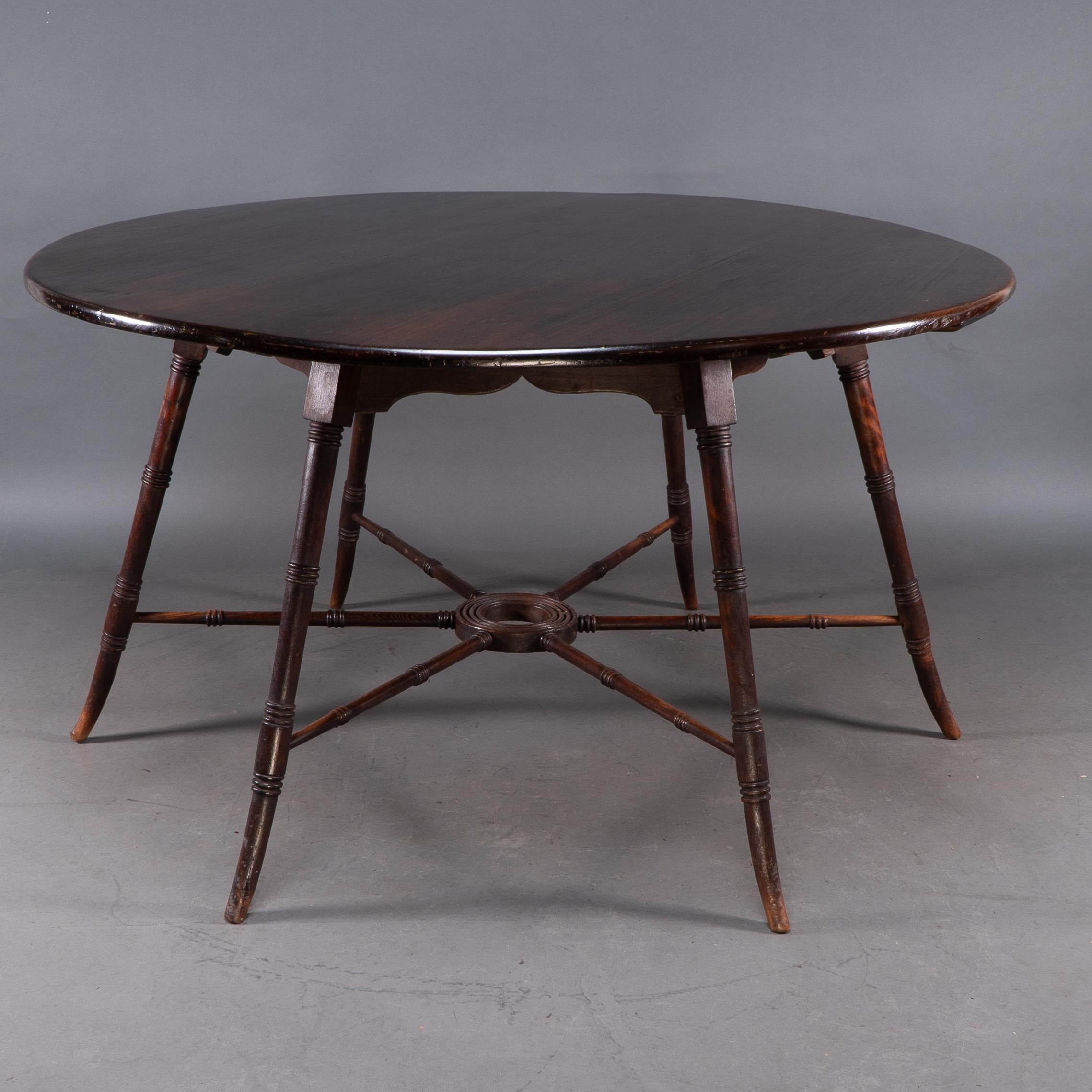 E W Godwin, attributed. Probably made by Collinson and Lock. 
An Anglo-Japanese Aesthetic Movement walnut centre or dining table, with a large circular top with a shaped apron below, on six flaring turned legs, united by six radiating spoke