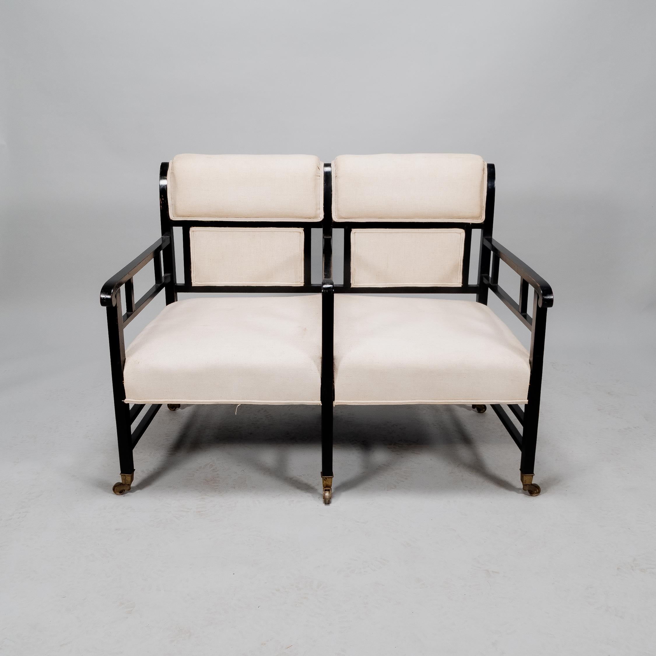 E.W. Godwin attributed, an Anglo Japanese ebonized duet or conversation settee with curved back rest, three dividing arms stood on six square legs united by twin stretchers and single stretchers to the back.