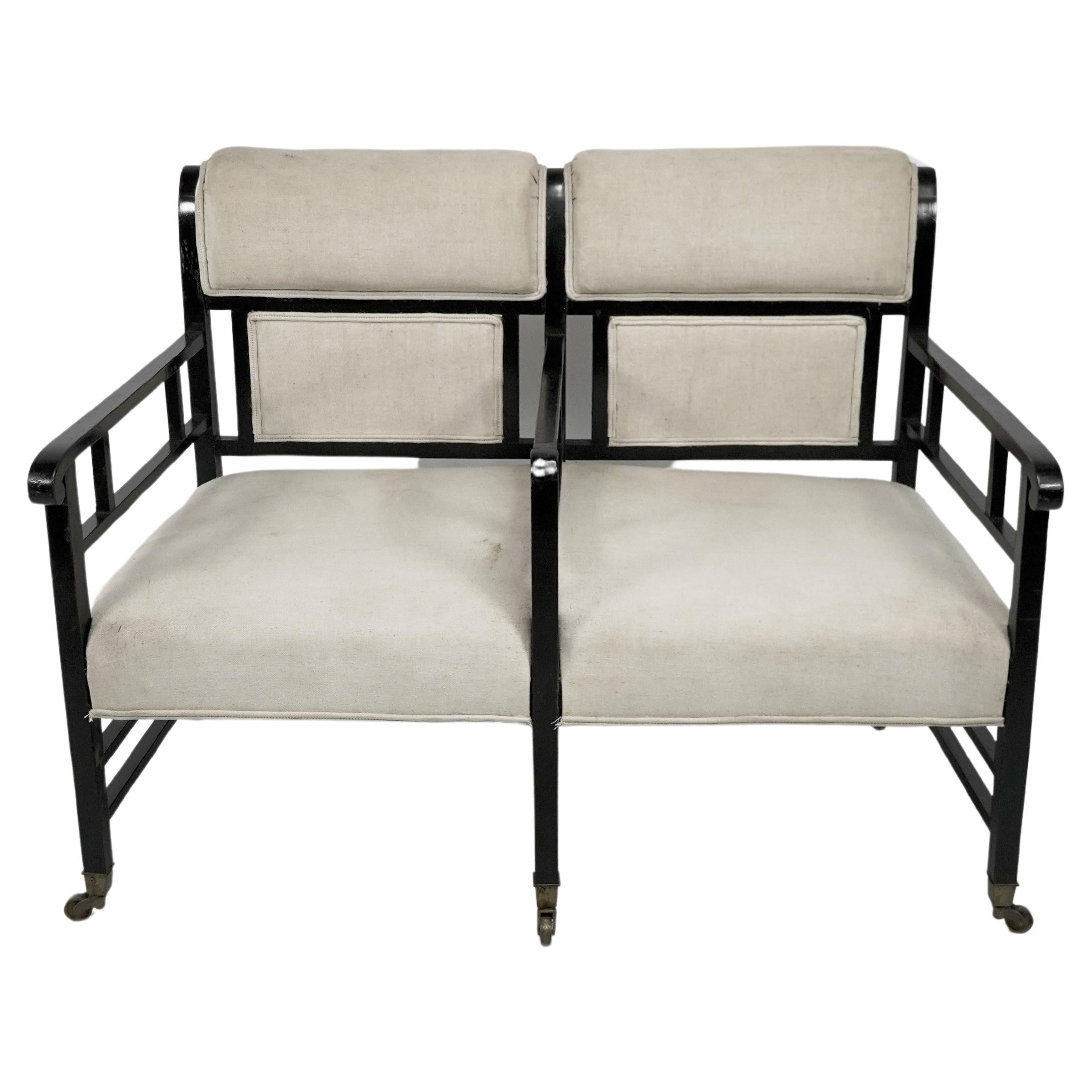 E.W. Godwin attributed, an Anglo Japanese ebonized duet or conversation settee with curved back rest, three dividing arms stood on six square legs united by twin stretchers and single stretchers to the back.