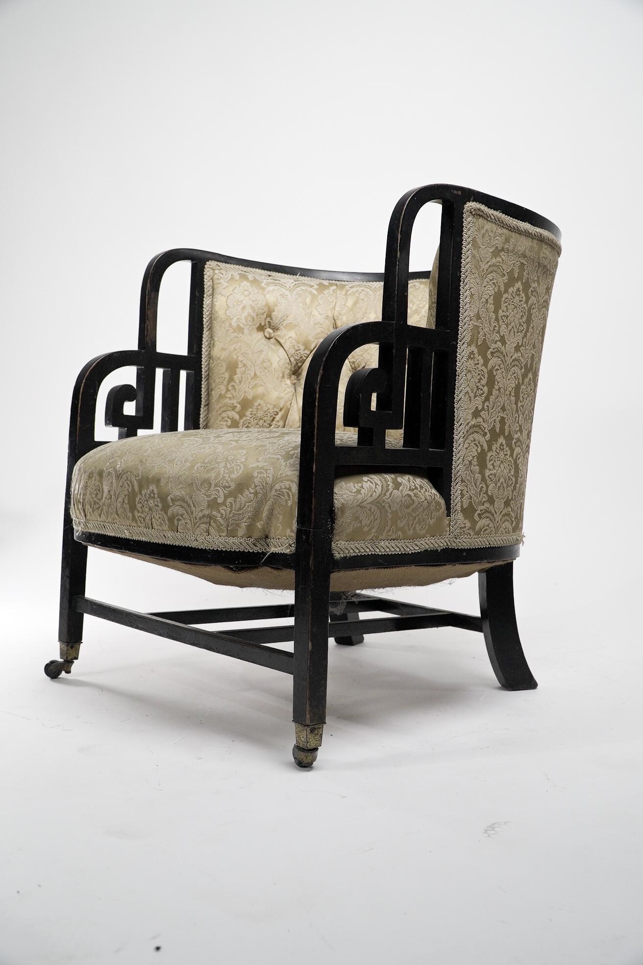 An Anglo-Japanese ebonised walnut lounge chair with stylised Greek key details to the arms and four lower stretchers uniting the legs. Original brass and ceramic castors.