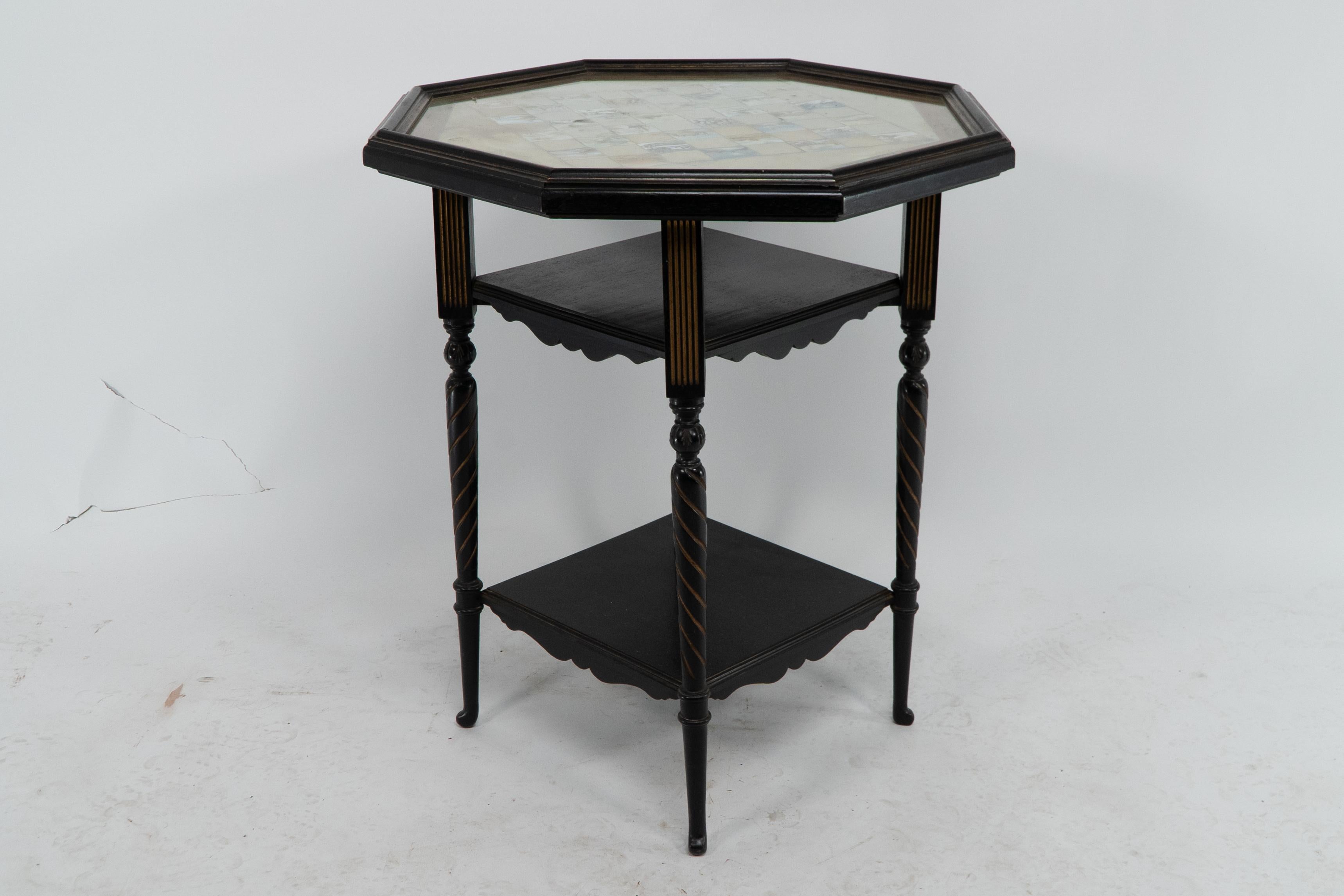 E.W. Godwin attributed for Collinson & Lock. An ebonized and parcel gilt side table chess table with hand painted scenes on silk under an octagonal glass top. The silk has a little watermark on the right-hand lower corner.