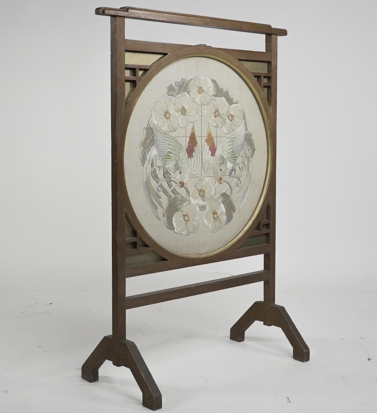 E W Godwin. In the style of. An Anglo-Japanese designed fire screen, with a stepped top rail and a Japanese silk embroidery depicting a pair of parrots or parakeets amongst floral decoration, set in a circular gilt edge frame with Japanese blind