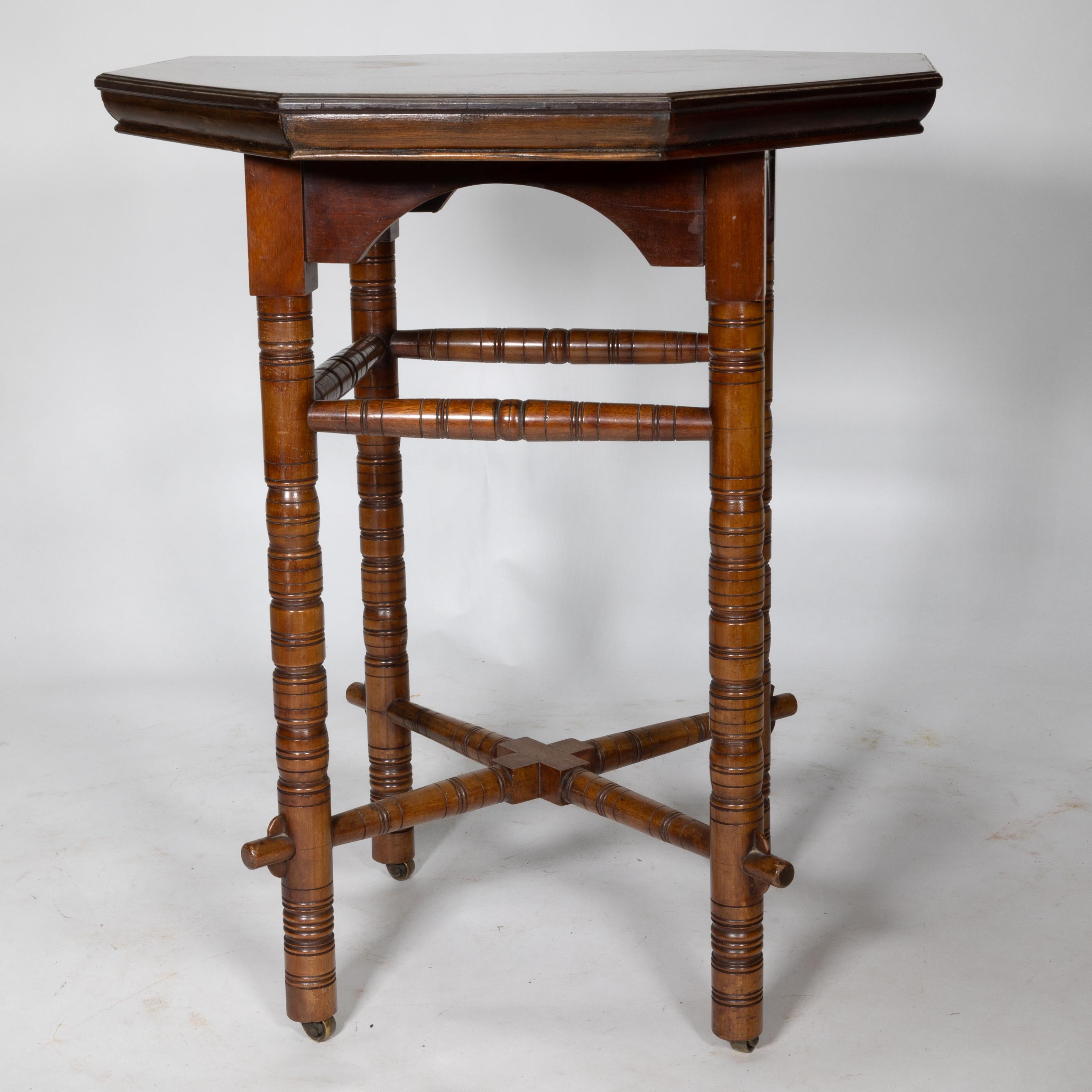 E.W. Godwin in the style of.An Aesthetic Movement Walnut octagonal centre or side table with arched apron below the top, the legs united by upper stretchers and also united by a lower a cross stretcher which follows through the lower legs with