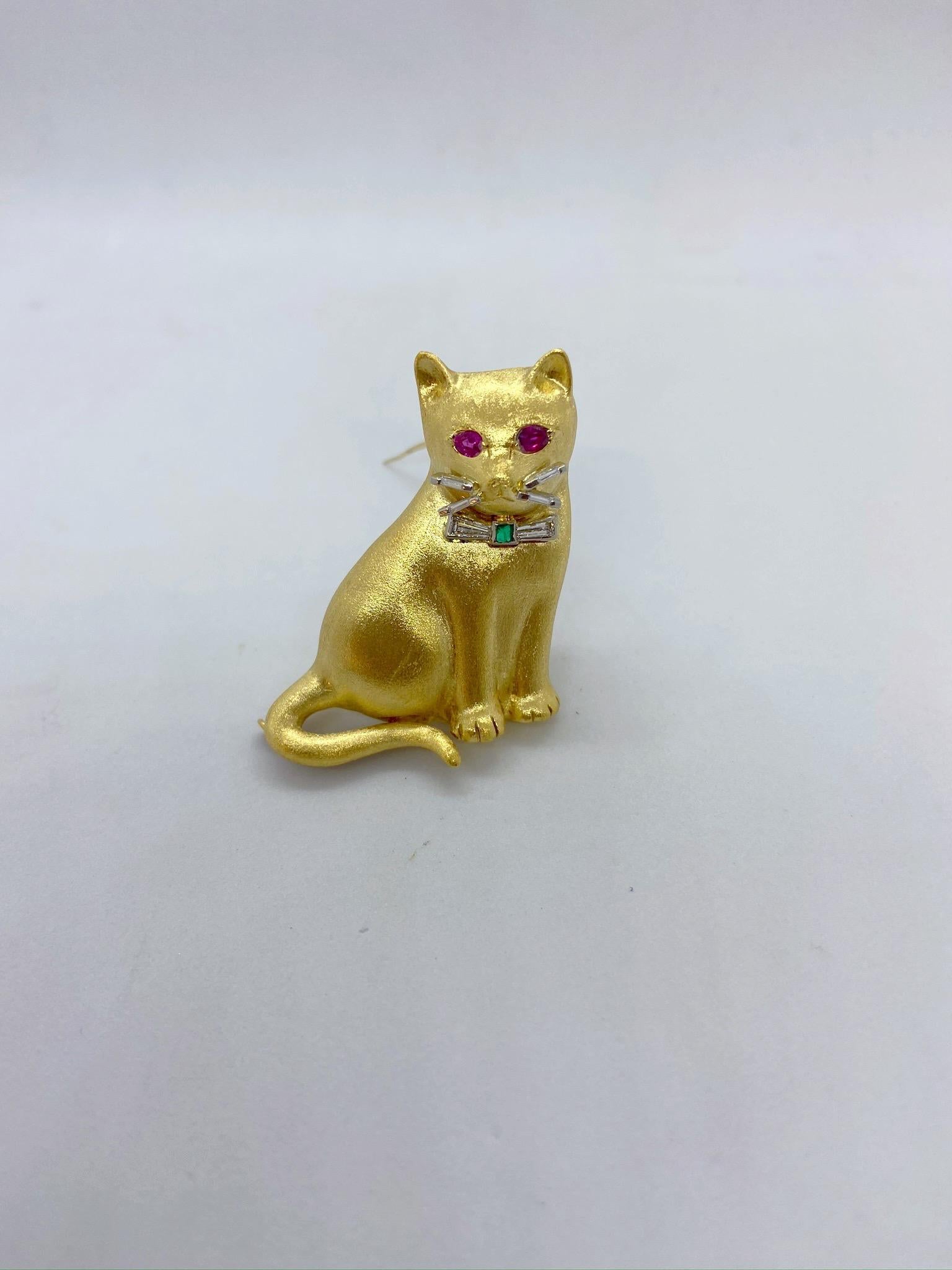 This magnificent 18 karat yellow gold cat brooch has a smooth satin finish, magically looking like fur. The adorable cat's features are uniquely designed with ruby eyes, and baguette diamond whiskers. His bow tie is set with a square emerald and