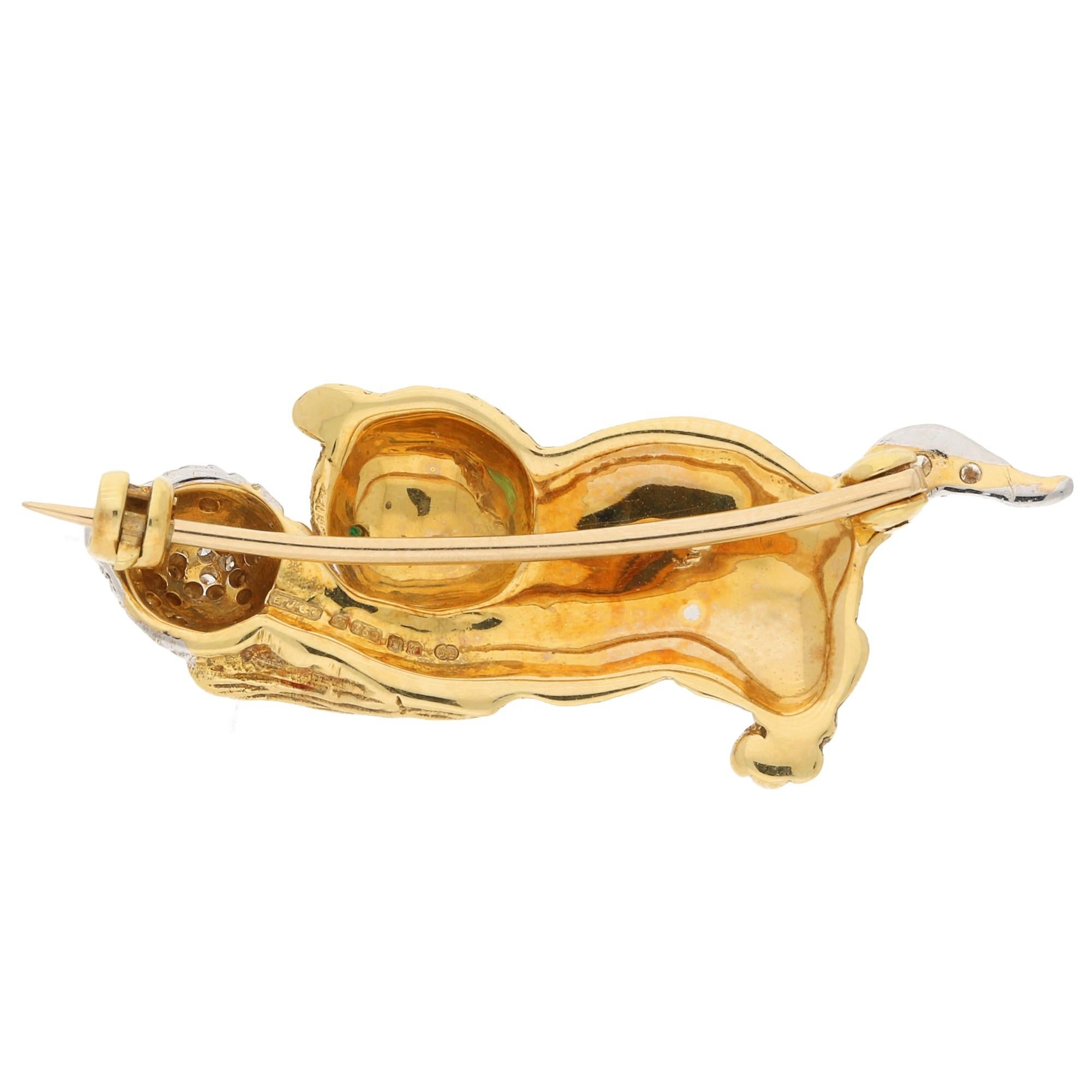 A delightful E. Wolfe & Co. vintage diamond and emerald playing cat brooch in 18-karat yellow and white gold, circa 1993. The brooch is designed as a cat playing with a ball, the cat displaying a hand-finished carved fur effect to the yellow gold