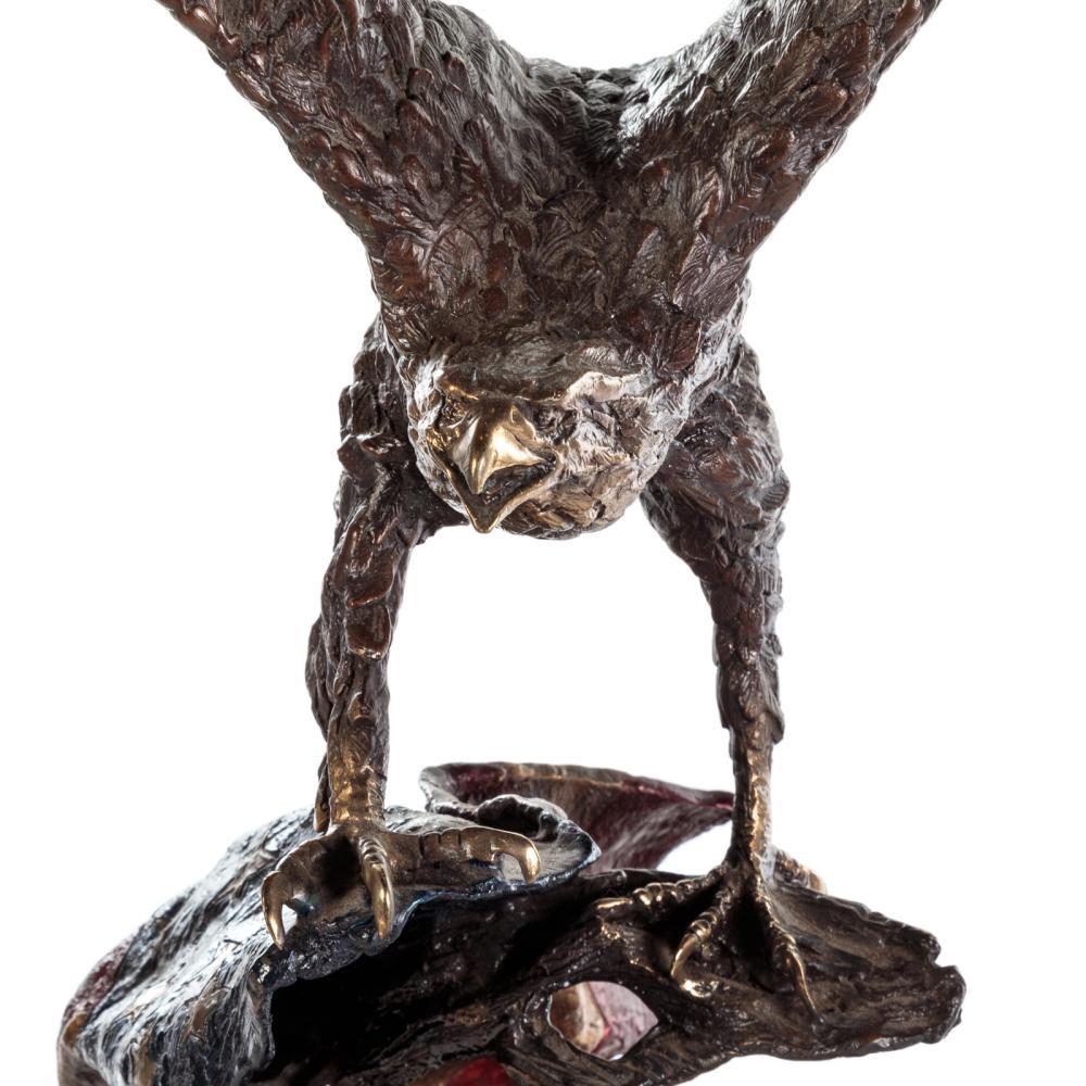 Präsentiert wird ein patinierter Bronzeadler von Lorenzo E. Ghiglieri. Der Adler ist mit dramatisch erhobenen Flügeln auf einem Baumstumpf landend abgebildet. Der Baumstumpf ist mit einer vielfarbigen amerikanischen Flagge drapiert. Die Bronze ist