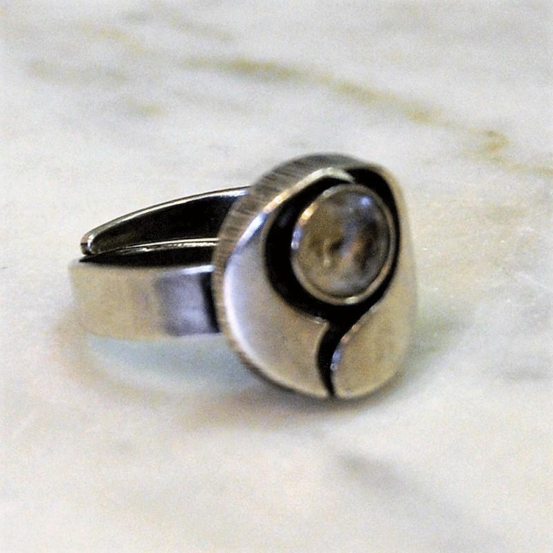 A nice silverring from year 1948 with a round brilliant cut rock crystal stone surrounded by a open frame with stripes on the sides. The ring is adjustable to fit any size. Marked 925 S P8.
Measure: Inner diameter is 17 mm, height of ring 23 mm,