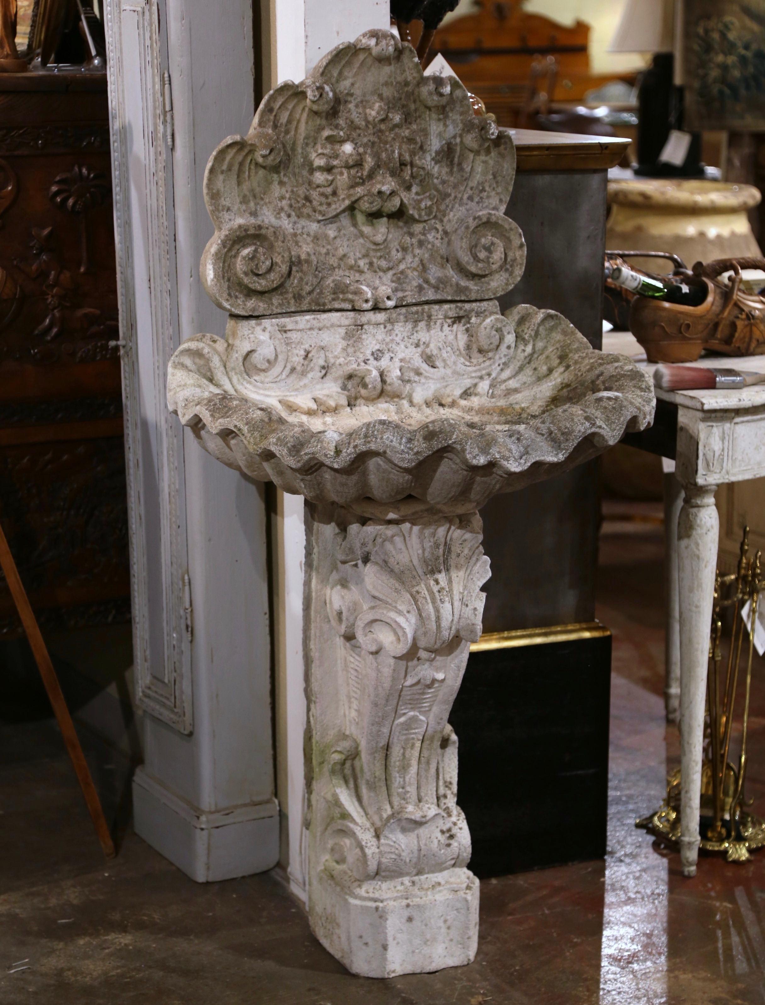 This elegant antique fountain was crafted in southern France, circa 1920. Carved of stone and built in three sections, the fountain features a carved base with volutes, decorated with shell and scroll motifs, over a demilune shell form basin; the