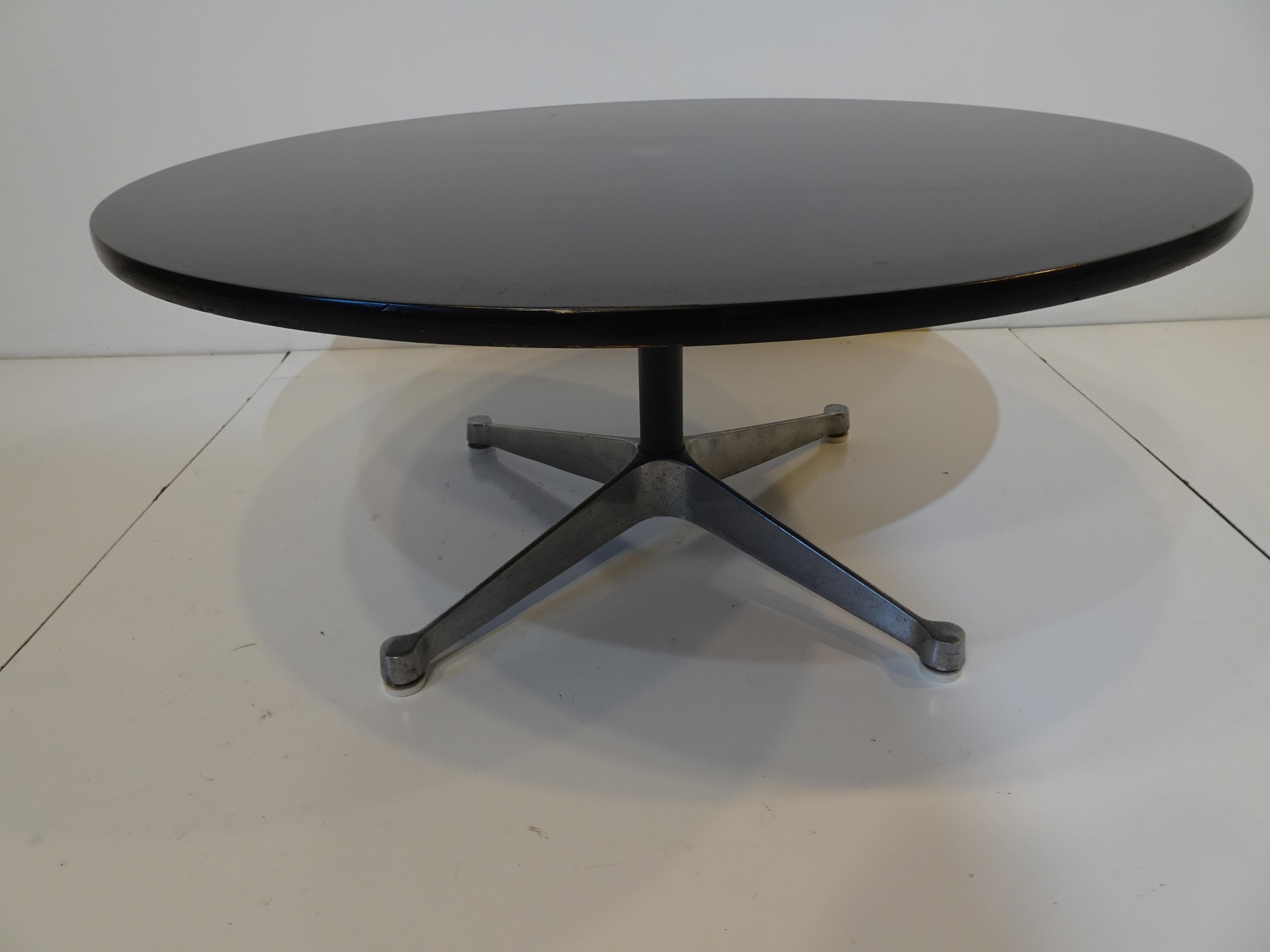 A satin black round wood coffee table with cast aluminum star base and adjustable plastic foot pads to protect your floors . A simple by strong design by Ray and Charles Eames for the Herman Miller Furniture Company from their Aluminum Group