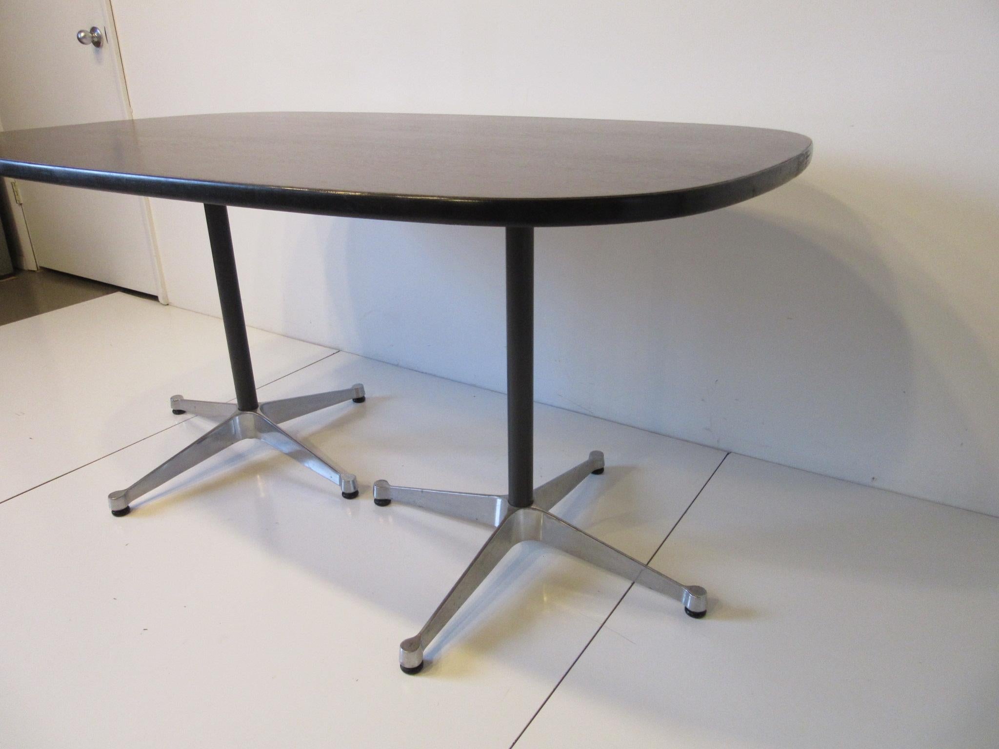 A nice sized medium ebony toned dining table with satin black edge having black pedestals attached to cast aluminum star bases with adjustable foot pads. Retains the labels designed by Ray and Charlies Eames for the Aluminum Group Collection