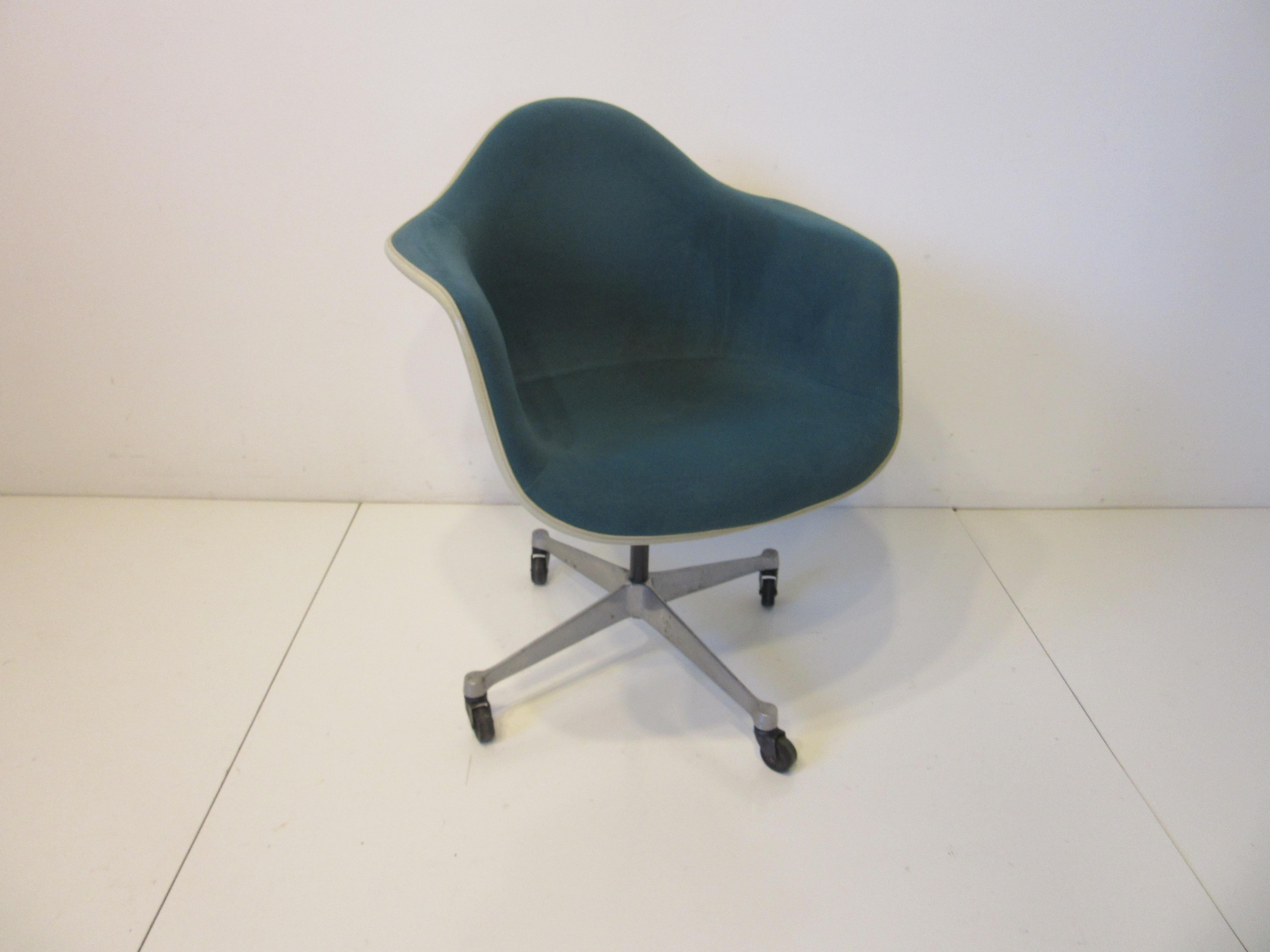 An upholstered Eames rolling arm shell desk chair in a medium aqua marine toned soft fabric with cream hard molded backside. The swiveling seat is supported by a satin black steel tube and sits on a four star cast aluminum base with black rubber