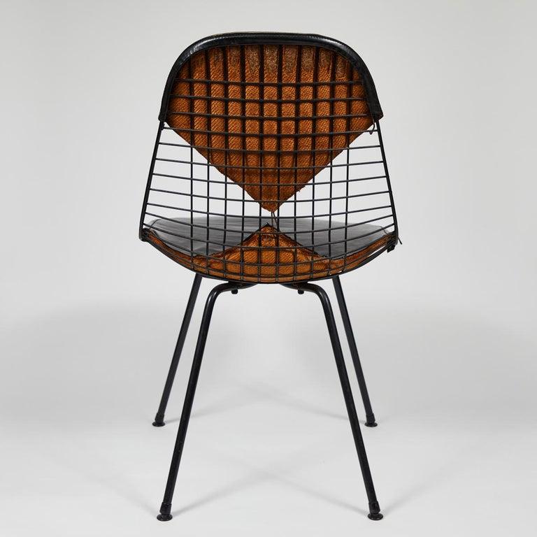 Iconic Eames Bikini chair in soft black leather. The mid-century classic features a sloping wire net seat-back, four slim metal legs set at a straight, slightly winged angle, and harlequin-cut vinyl upholstery. A stylish and timeless addition to any