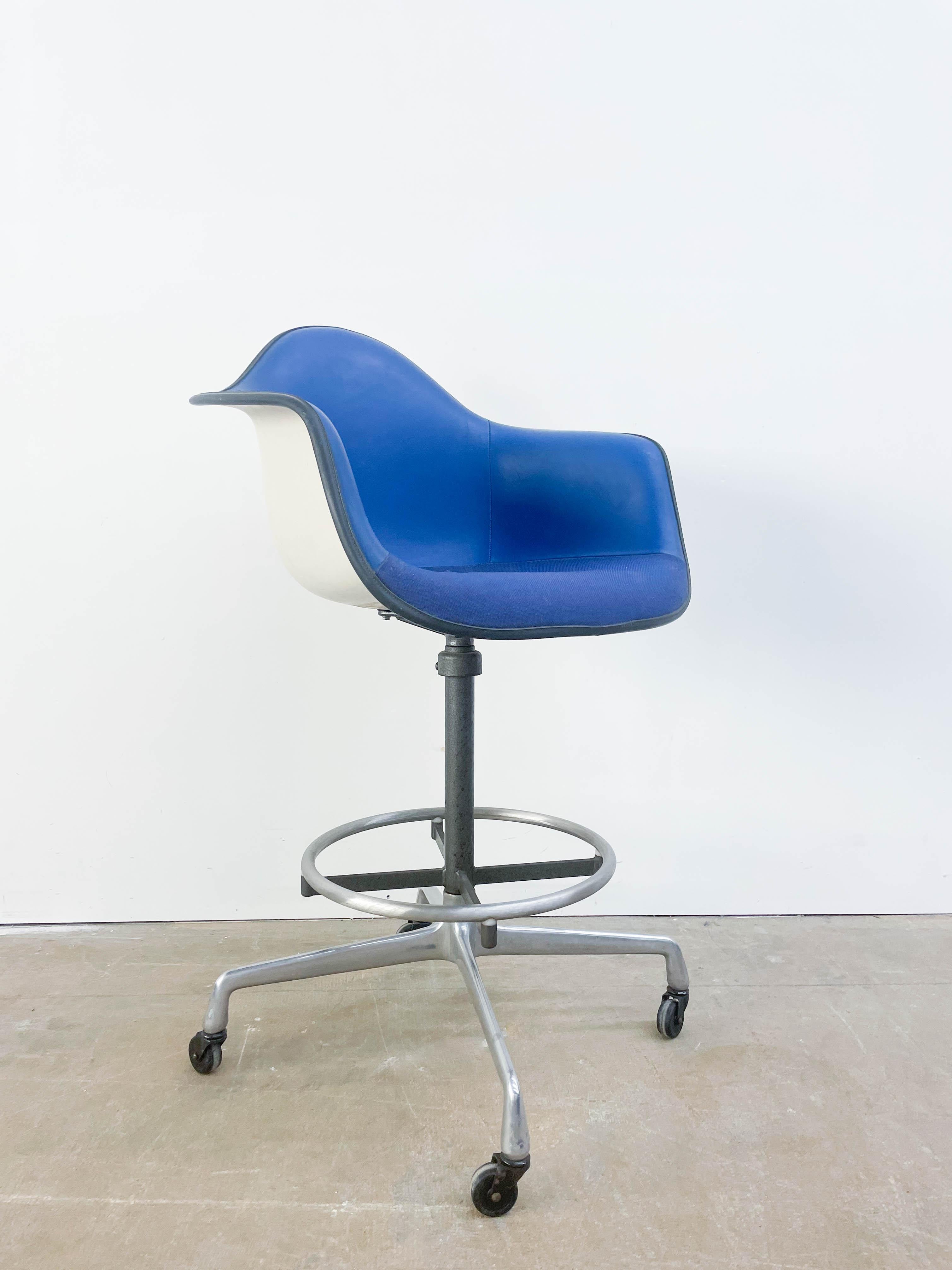 Blau gepolsterter Eames-Stuhl auf hohem Designer-Drehfuß mit Rollen. Dies ist eine ungewöhnliche und auffällige Kombination aus Komfort und Funktionalität.
  