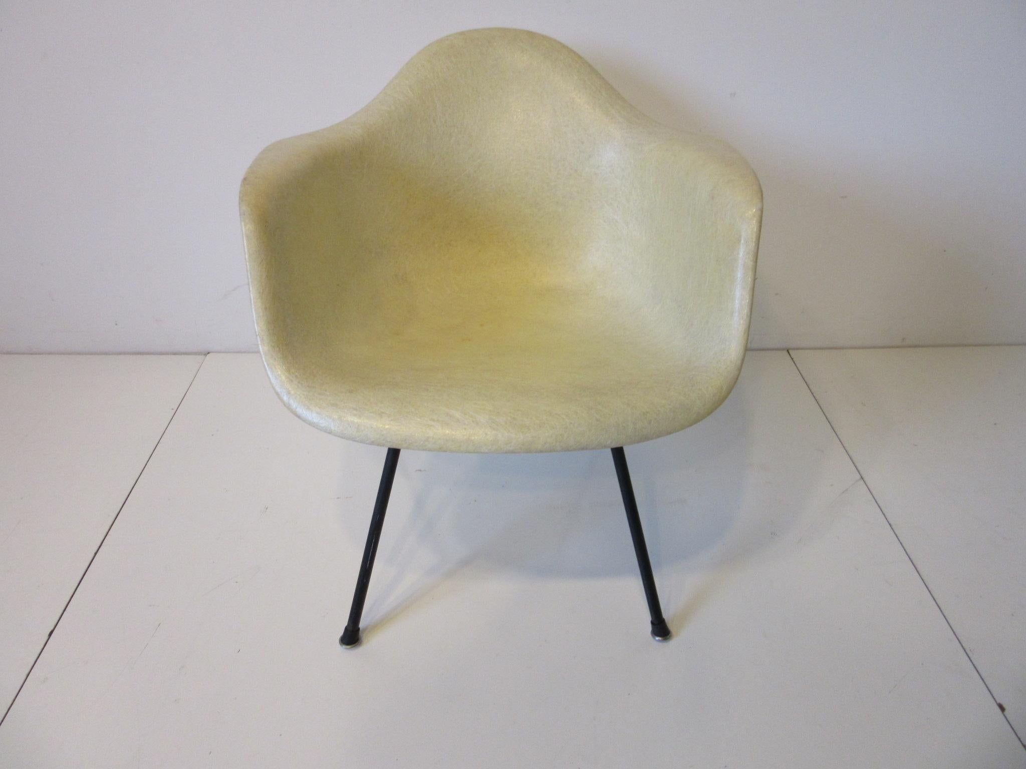 An early second generation parchment fiberglass arm shell chair with large shock mounts and black iron base in the rare lower lounge height . Having slip on black boot feet of rubber and metal manufactured by the Herman Miller Furniture company in