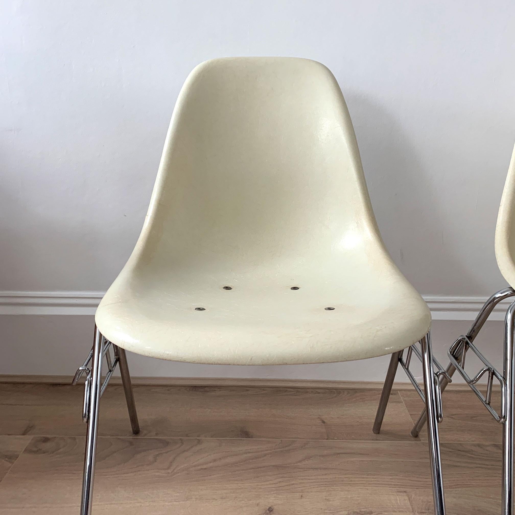 An iconic pair of parchment coloured fibreglass shell chairs on stacking bases, designed by Charles and Ray Eames for Herman Miller.