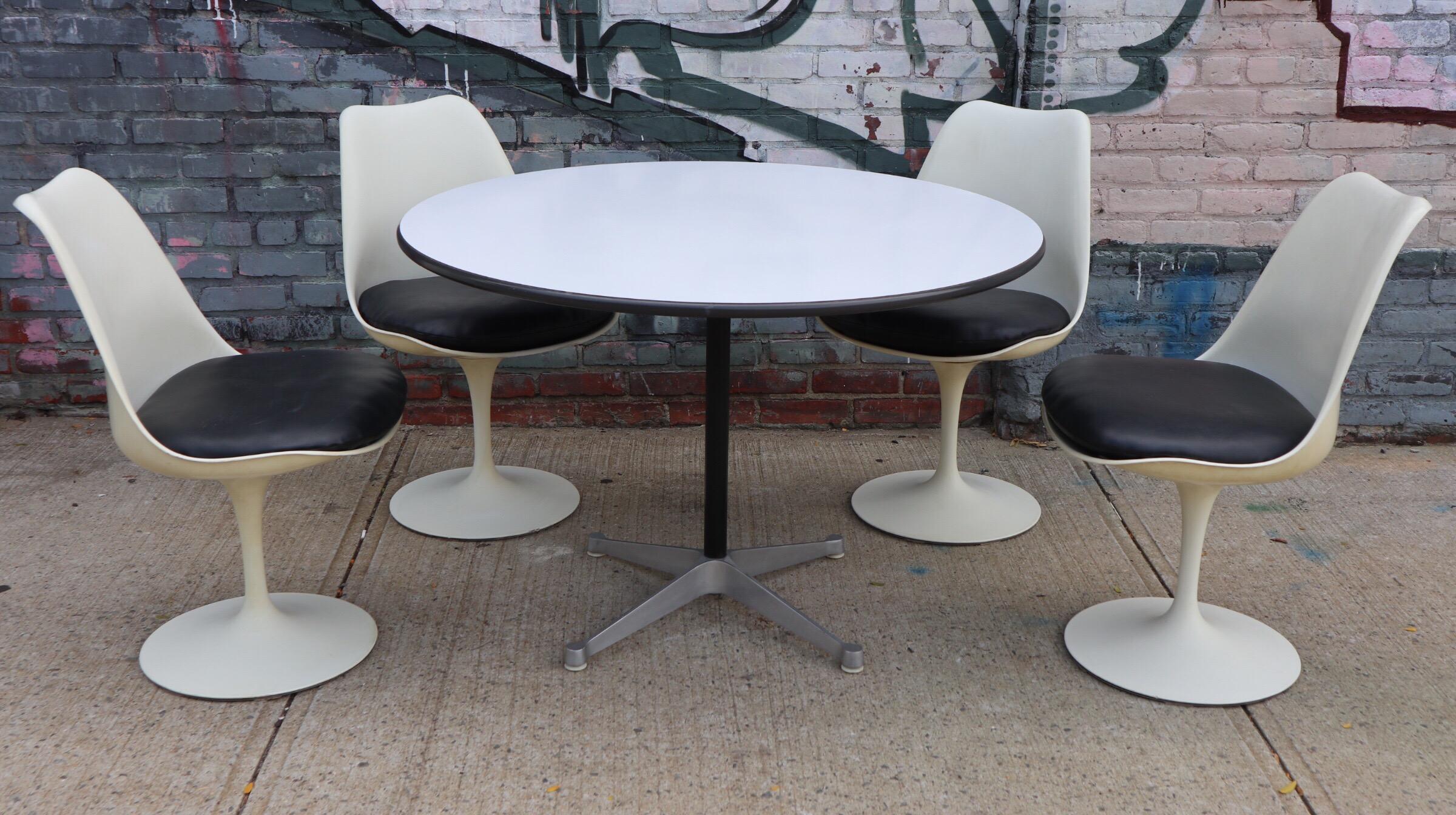 Dining set consisting of table and 4 tulip chairs by the iconic American designers Charles and Ray Eames and Eero Saarinen. The table has a top of white laminate in very good shape on aluminum four pronged base. Base retains all 4 glides and Herman