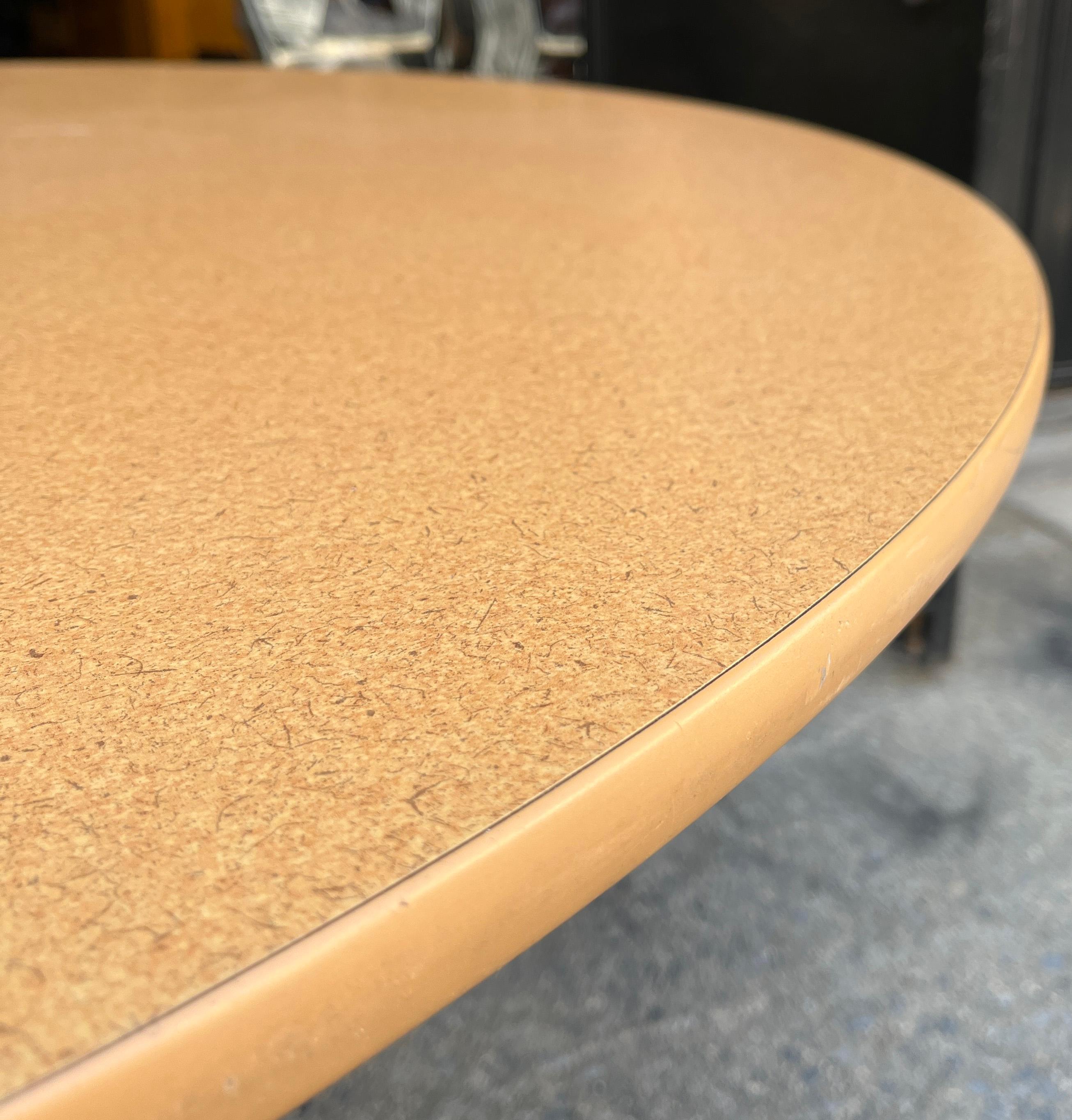 A post modern take on a classic design. Eames Aluminum group dining or conference table with an 80's take. Stunning cork laminate top with almond edge banding makes this table very durable. Single tone aluminum colored base with foot glides that