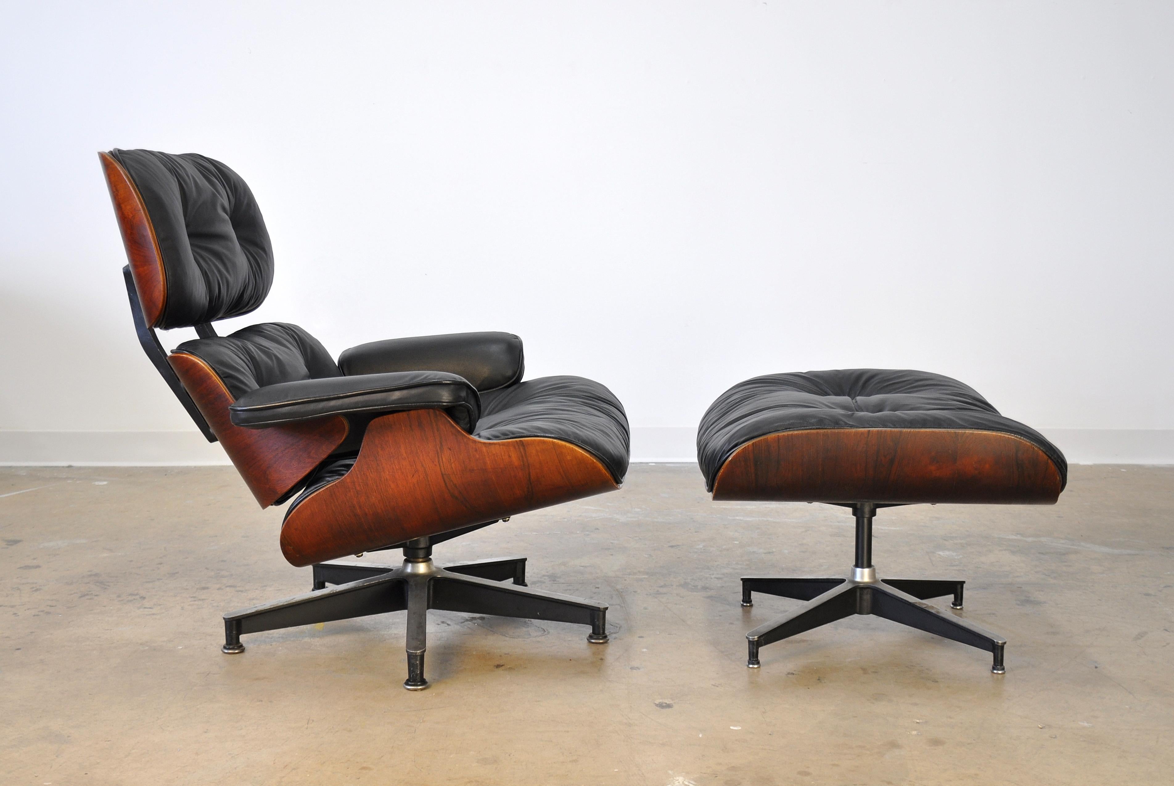 Iconic Mid-Century Modern black leather 670 lounge and 671 ottoman designed by Ray and Charles Eames for Herman Miller, dating from circa 1959. The swivel armchair and fixed footstool feature rosewood shells with tufted black leather and down