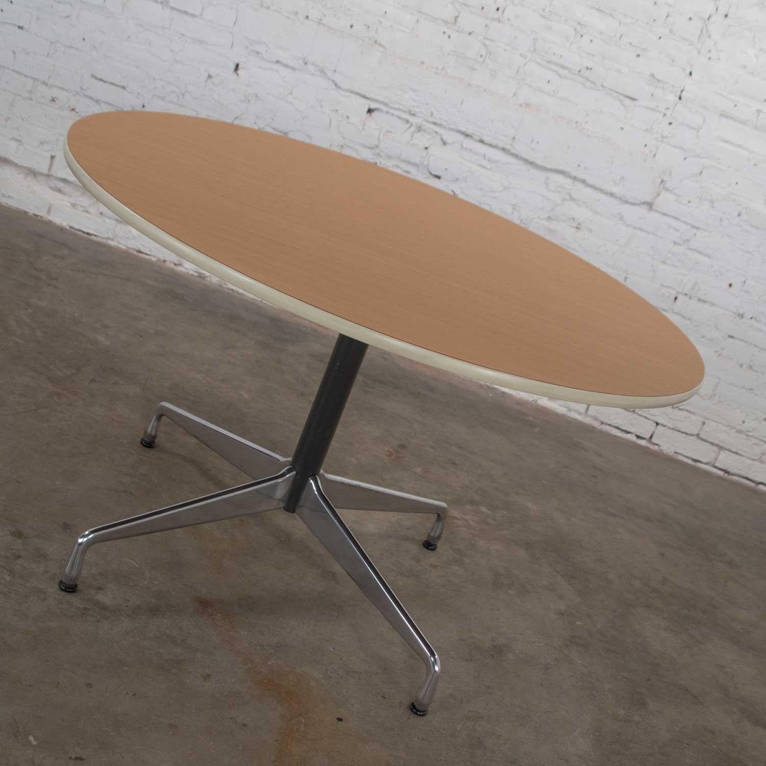 Renowned Eames Herman Miller round table with the universal base and a wood grain laminate top with off white edge trim, black painted shaft, and polished aluminum base. Wonderful vintage condition with no outstanding flaws that we have detected.