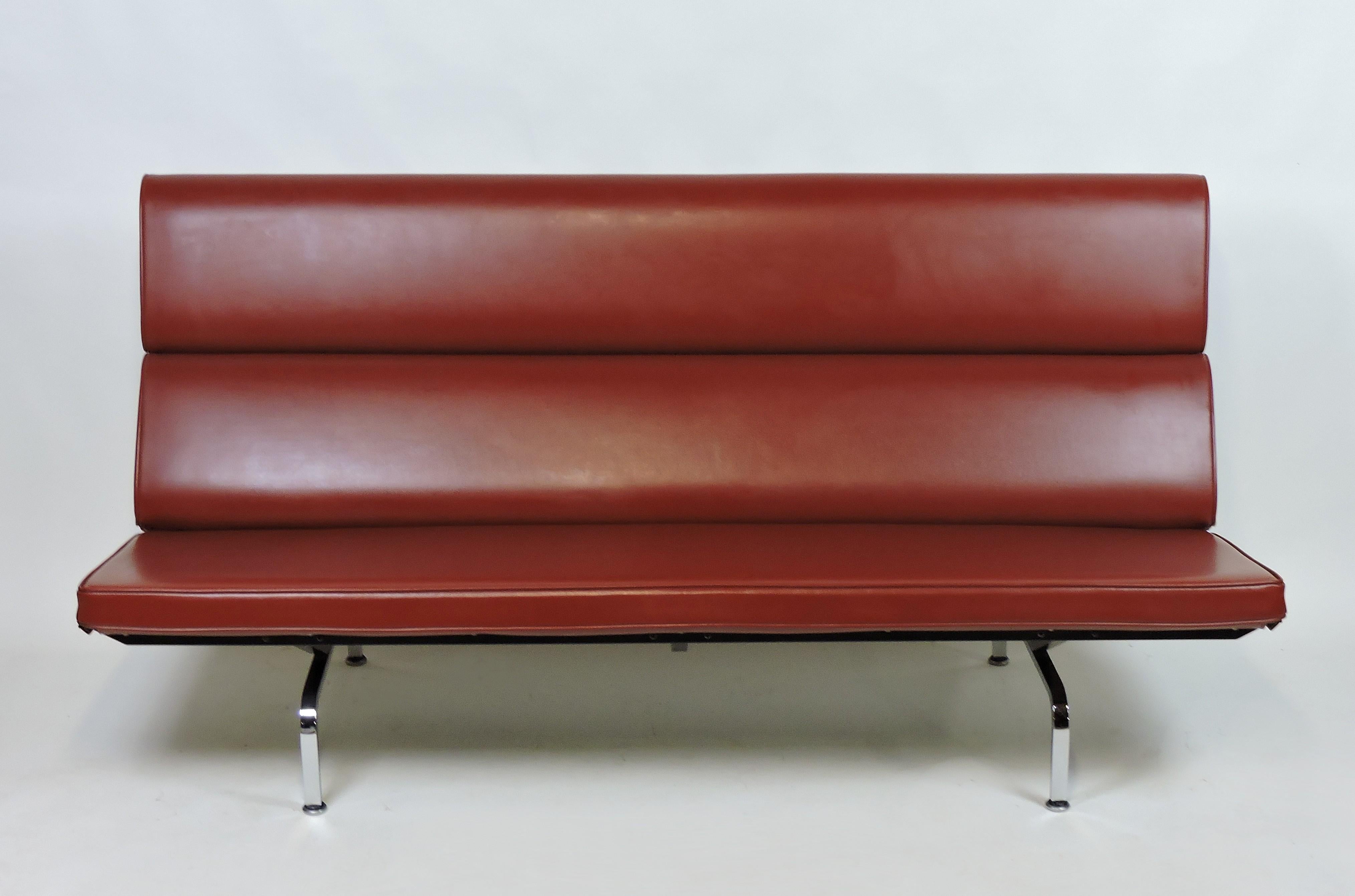 Sleek and handsome iconic compact sofa designed by Charles and Ray Eames and manufactured by Herman Miller. Upholstered in a dark red Naugahyde, this very comfortable sofa does not fold down like earlier versions. Labeled with the Herman Miller