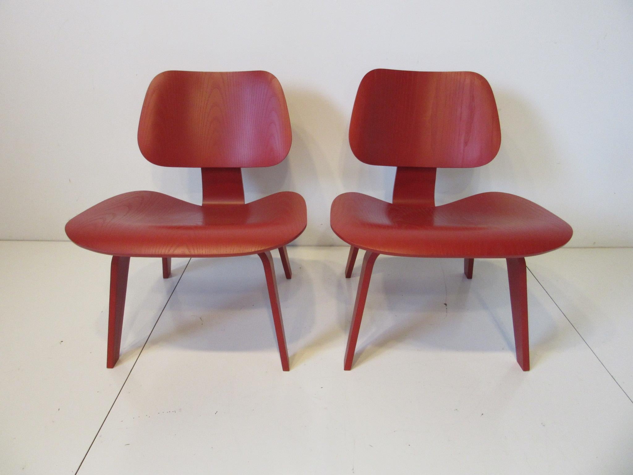 A matching pair of red dyed LCW lounge chairs in wood having the lower lounge height for comfort, continued production since the 1950's these iconic chairs are still as fresh as the first days of their introduction. Retaining the manufactures labels