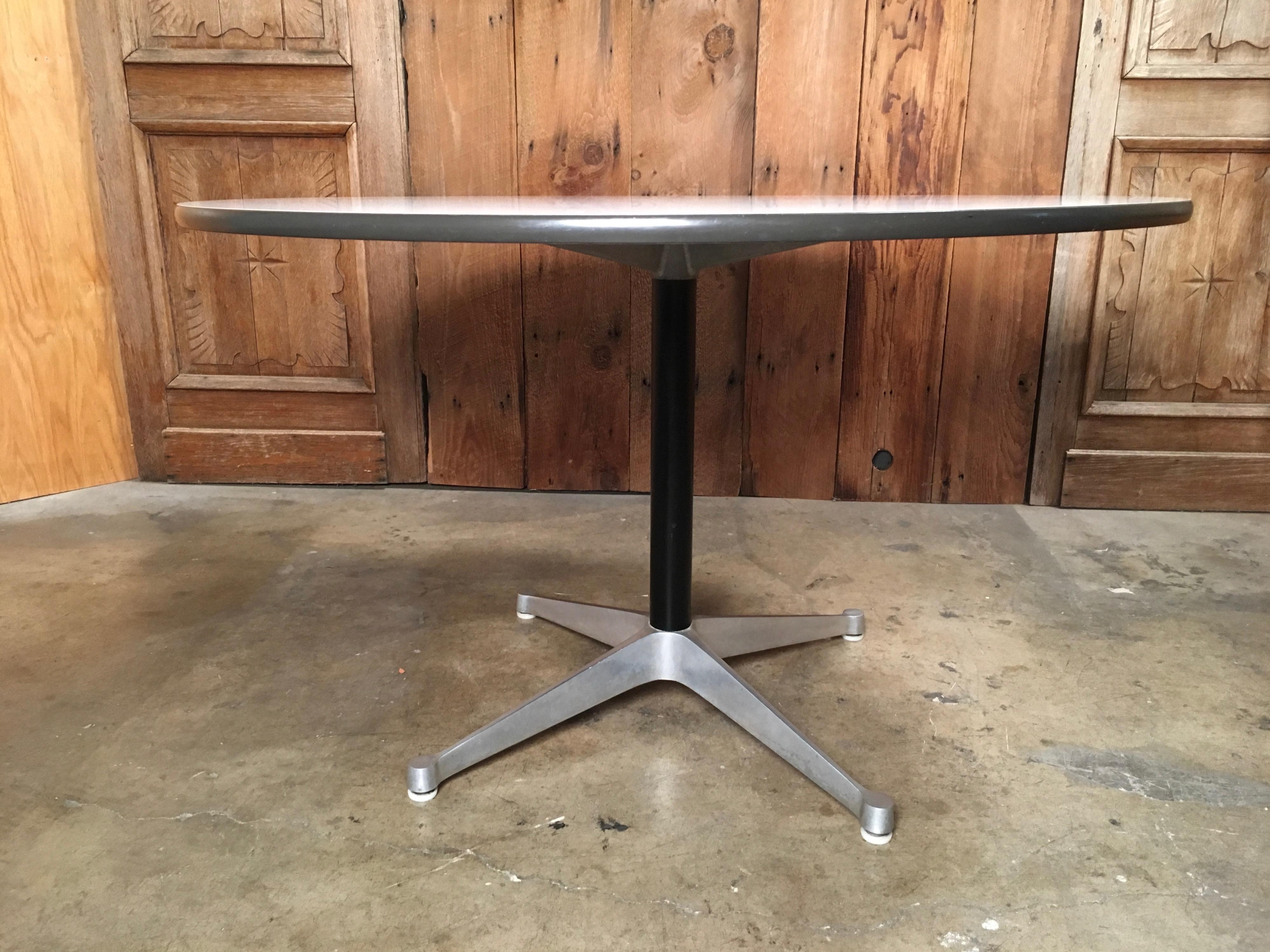 Charles and Ray Eames for Herman Miller white top and cast aluminum dining table. Featuring a round thick natural textured surface, black column on cast aluminum pedestal legs. . Herman Miller label to underside.