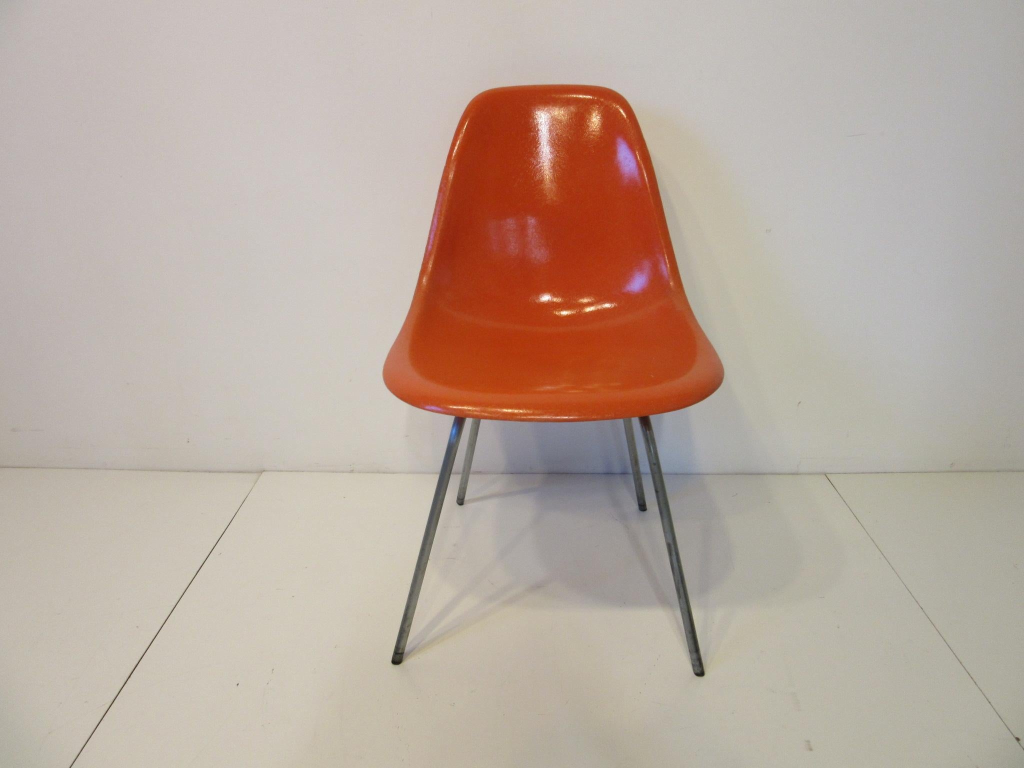 A set of four matching early orange fiberglass side chairs with zinc coated metal H bases and smaller black plastic tipped foot pads. Retains the paper manufactures label by the Herman Miller Furniture company Zeeland, Michigan.