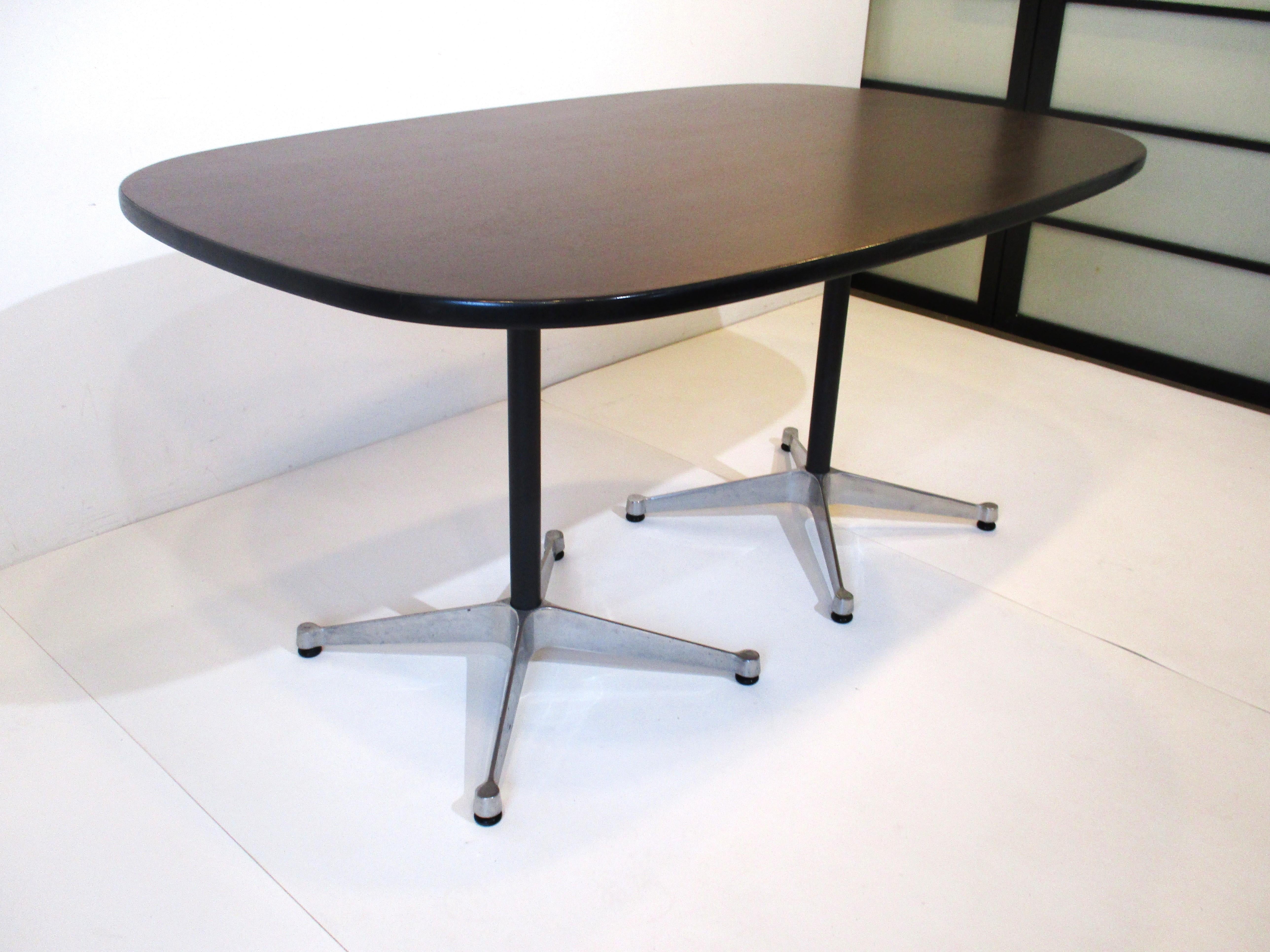 A smaller scale dark walnut topped dining table or desk with black rubber edge and double pedestal star base . From the Aluminum Group collection by the Herman Miller furniture company the bases are cast aluminum with satin black metal poles.