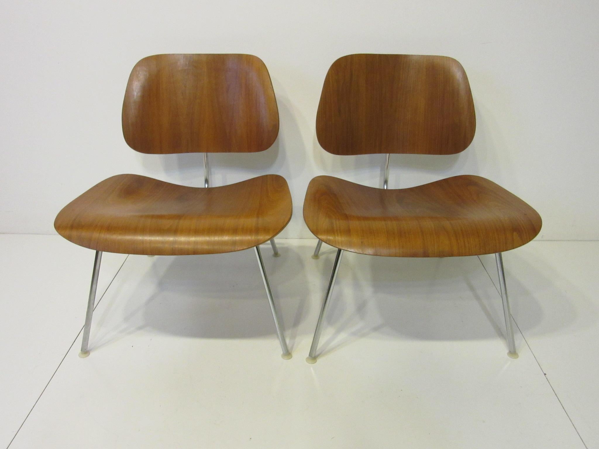 A matching pair of Eames LCM lounge chairs with rich walnut, chrome frames and plastic foot glides. Retains the manufactures labels and ink stamps by the Herman Miller Furniture Company.