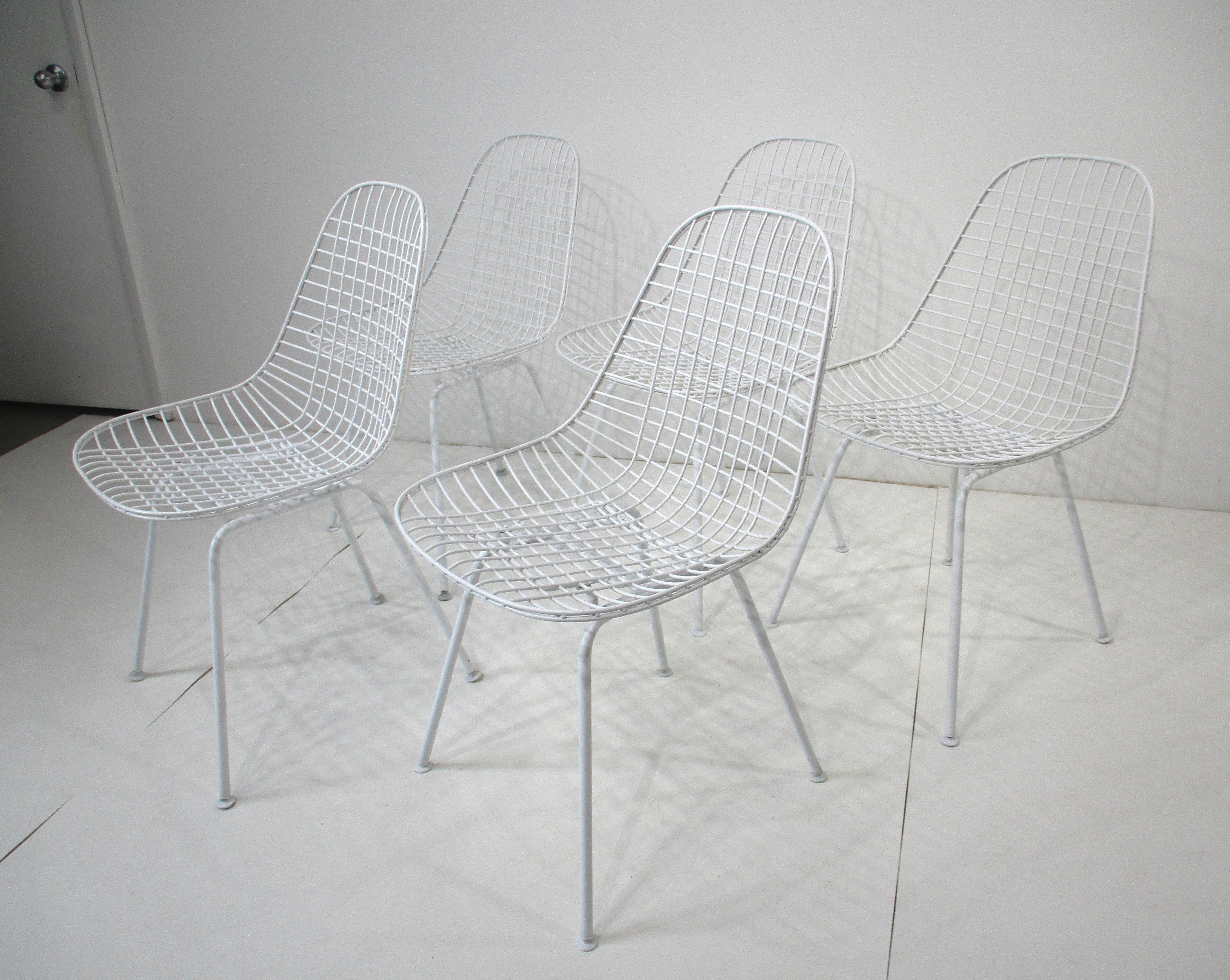 Un set di cinque sedie da pranzo a conchiglia in filo di ferro bianco con gambe a forma di H. H. dotate di pad in plastica per proteggere i pavimenti. Disegnato da Ray e Charles Eames, l'iconico team di marito e moglie le cui forme intramontabili