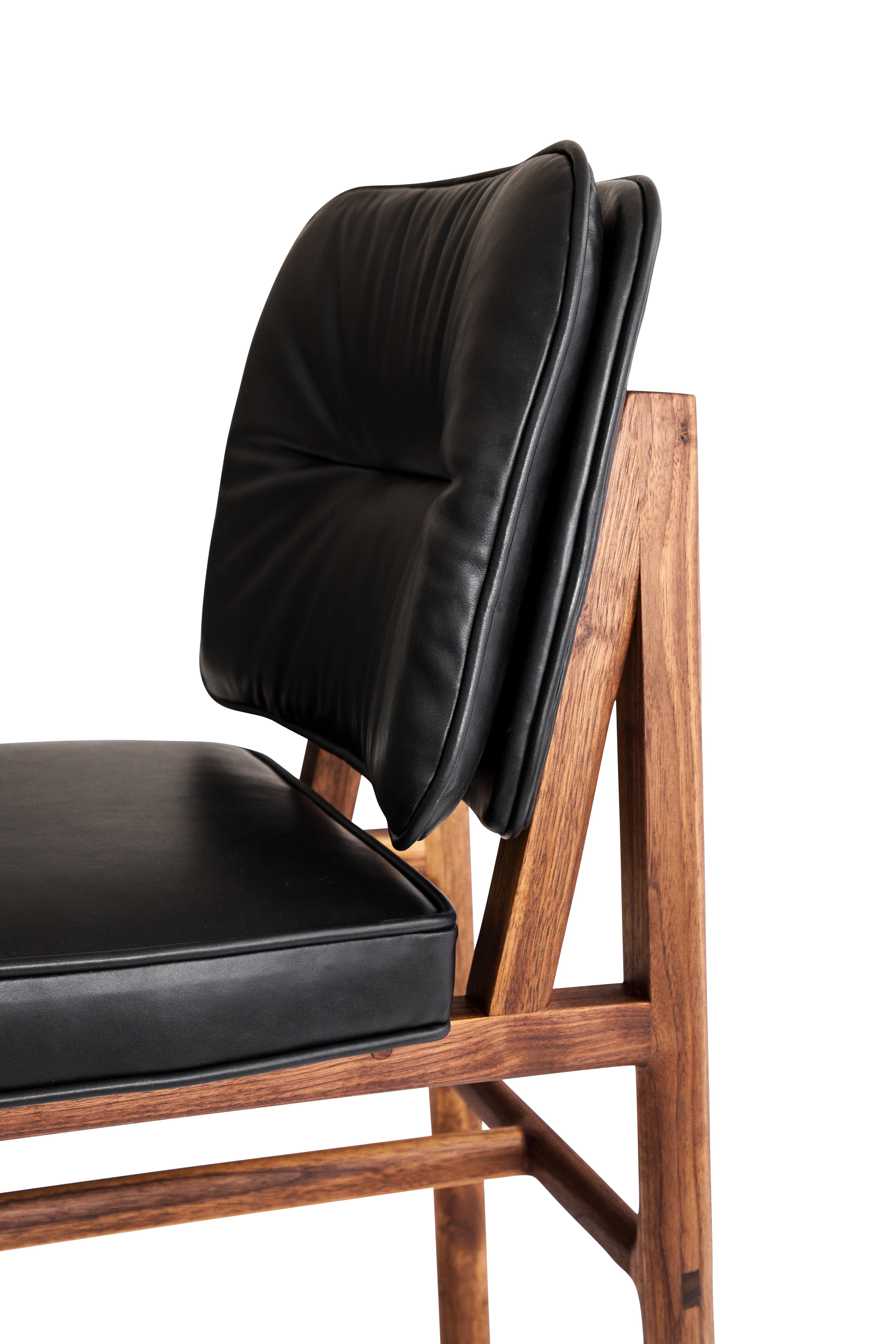 Massivholzkonstruktion mit handgeschnittenen Tischlerarbeiten und individuell gepolstertem Sitz und Rückenlehne. Dieser Stuhl ist in Nussbaum und schwarzem Leder gehalten.

Vorrätige Lederauswahl: schwarz, oliv, camel oder vegtan Leder.
Holzauswahl: