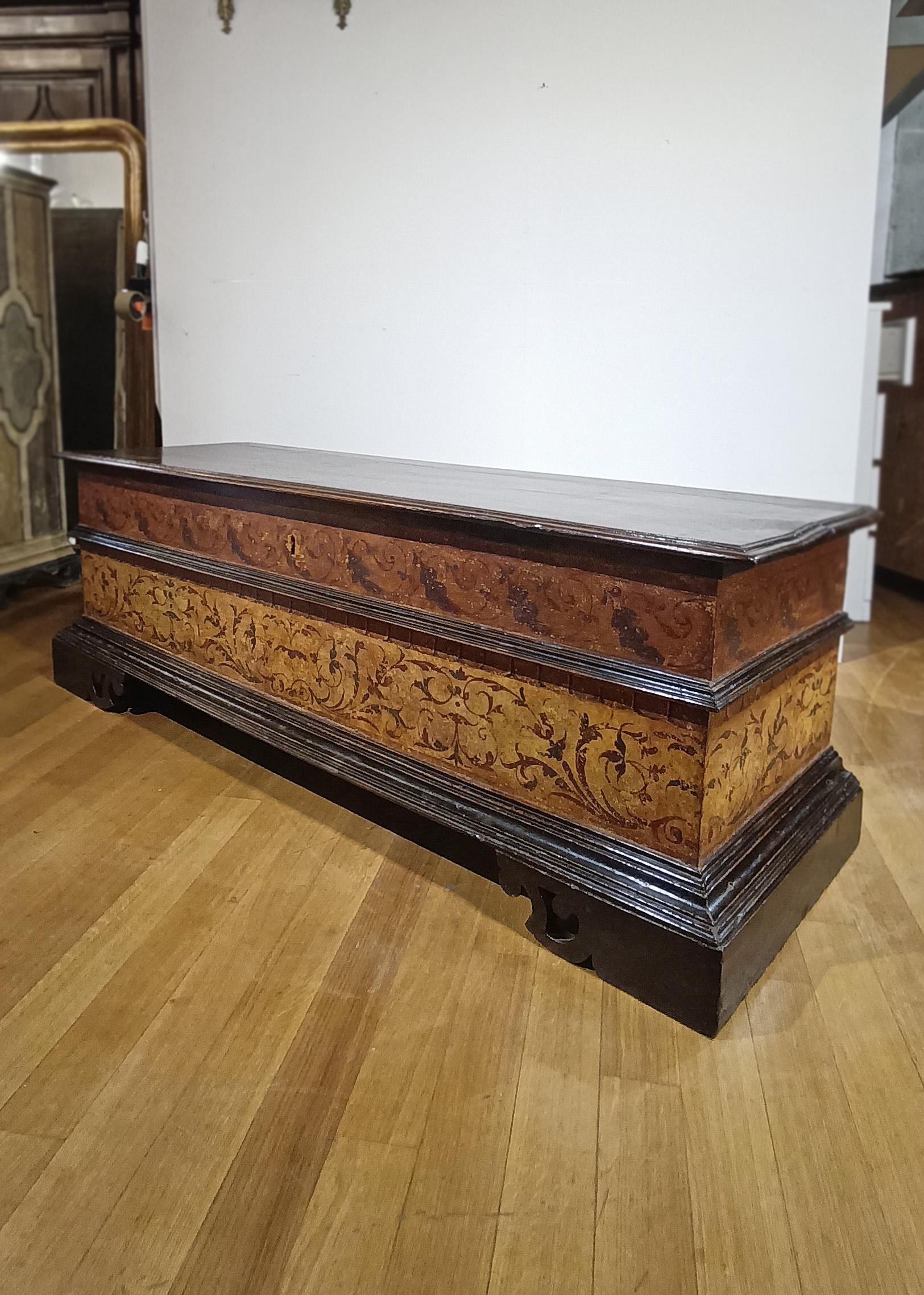 Elegante arcón de nogal macizo tallado y pintado. La arqueta tiene forma rectangular, con patas ménsulas, parte superior saliente y banda moldurada. La parte superior se abre, revelando un amplio espacio de almacenamiento. Su rasgo distintivo reside