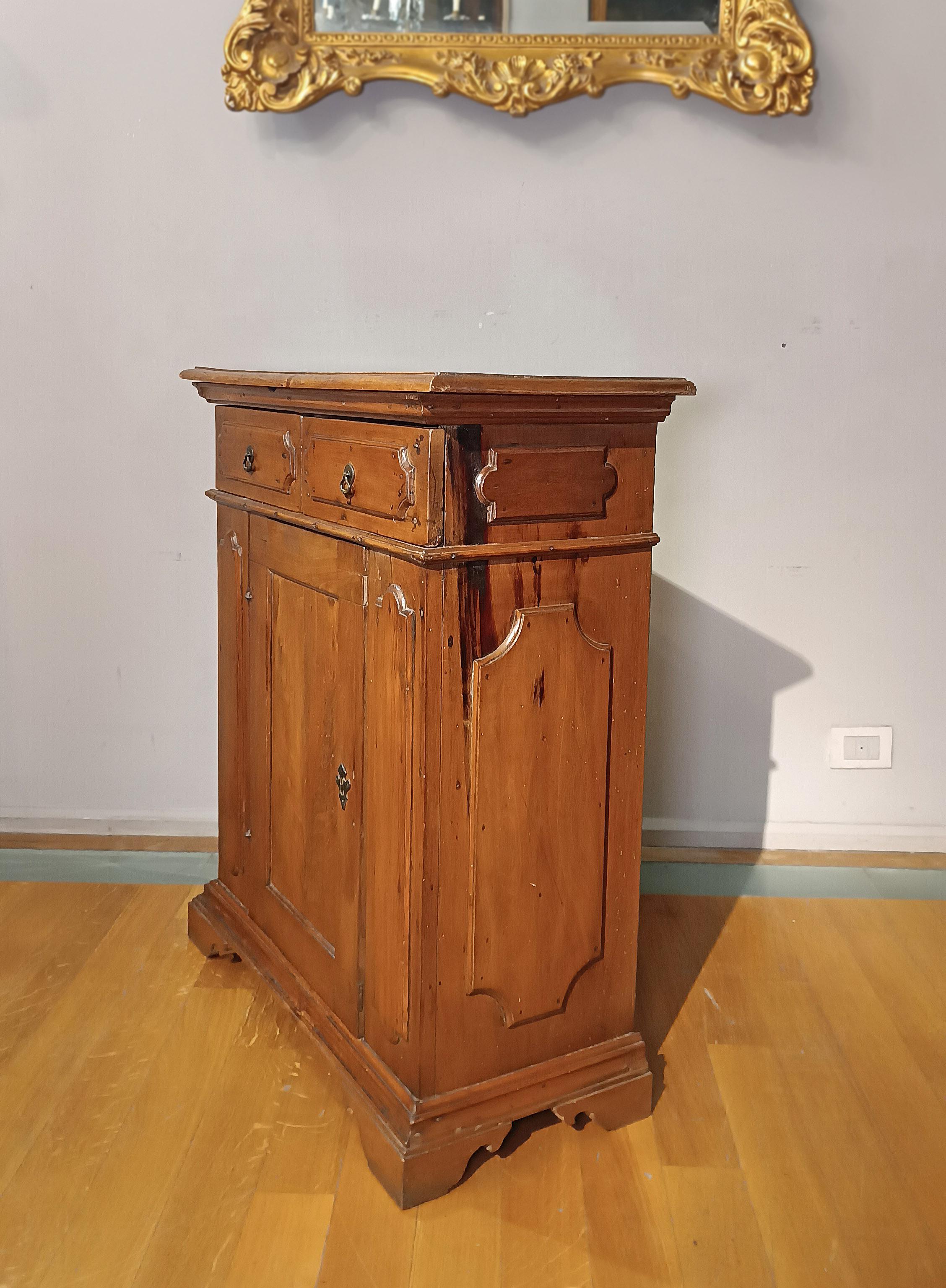 Elegant and refined sideboard in solid light walnut, finely carved. This piece of furniture, with its small dimensions, is equipped with a door and two practical front drawers, ideal for storing objects with ease. The bracket feet guarantee a solid