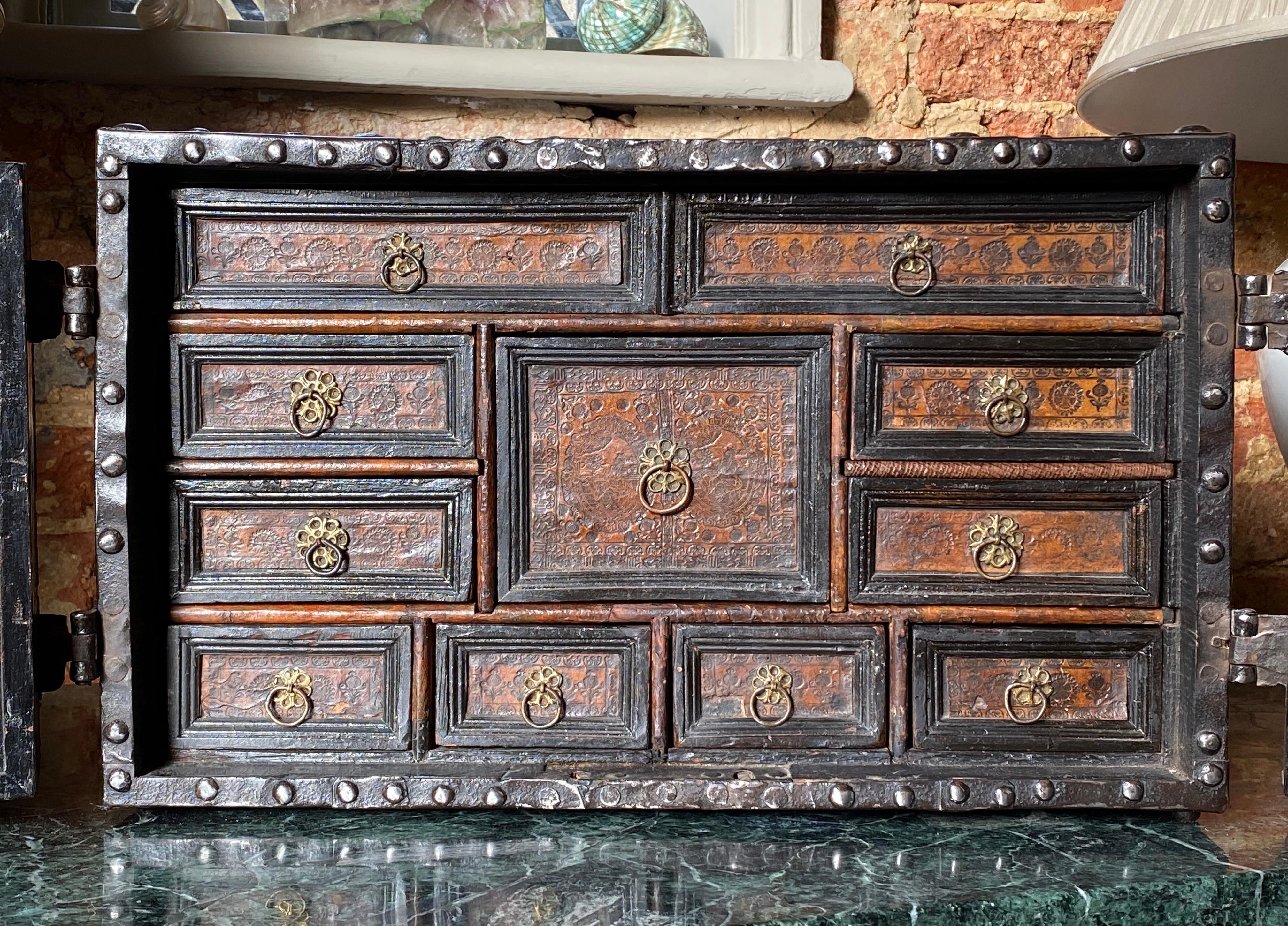 A steel-mounted strong box table cabinet, circa 1600.
Continental, probably French.

An ornately engraved antique steel-bound rectangular strong box, with front opening doors revealing numerous fitted drawers, concealing two secret compartments.