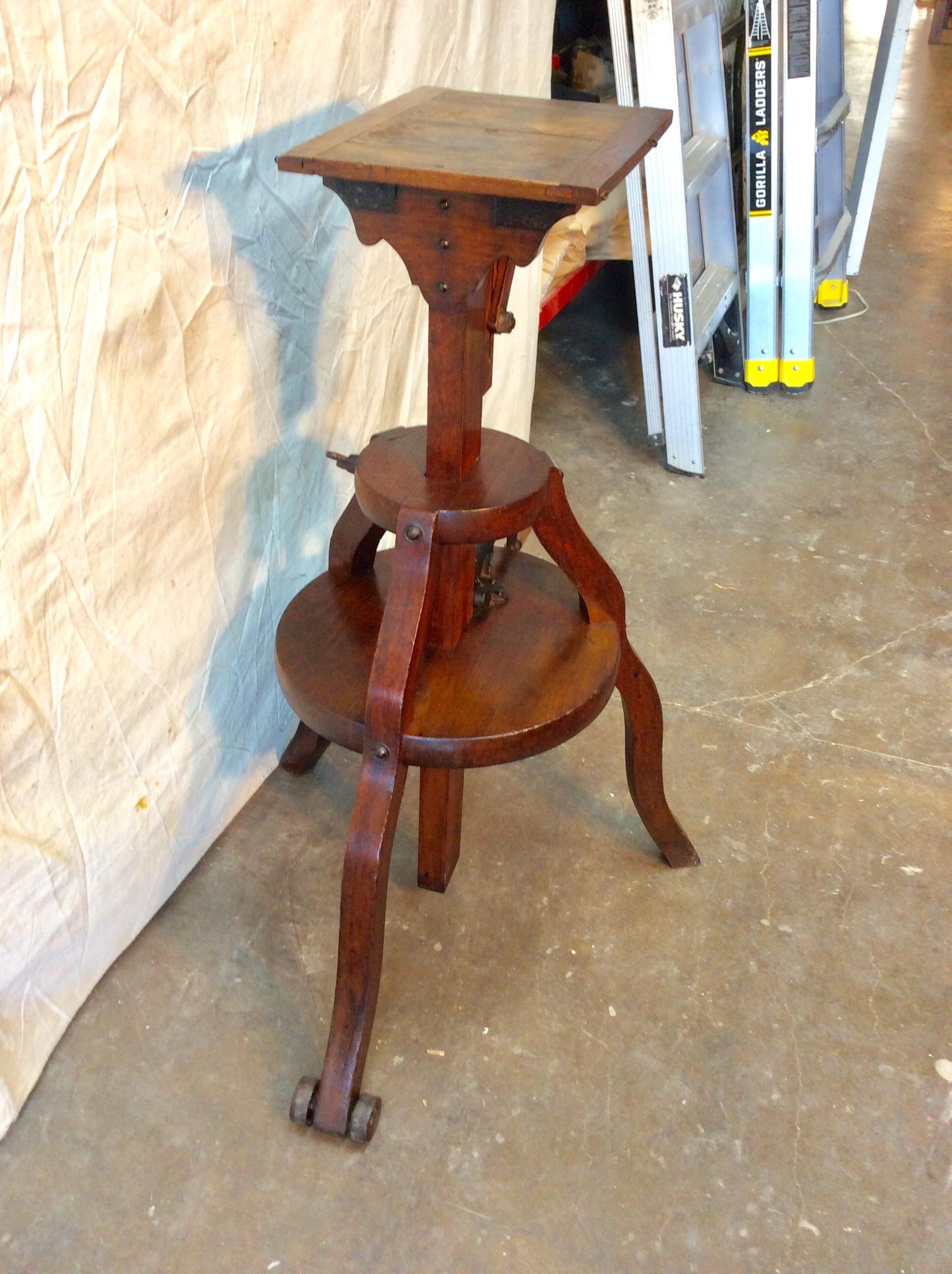 Found in the South of France this Early 1800s French Walnut Camera Stand is in good working condition. The piece features three curved legs which support a wood handled iron crank system to adjust the height of the stand. There is an iron wheel on