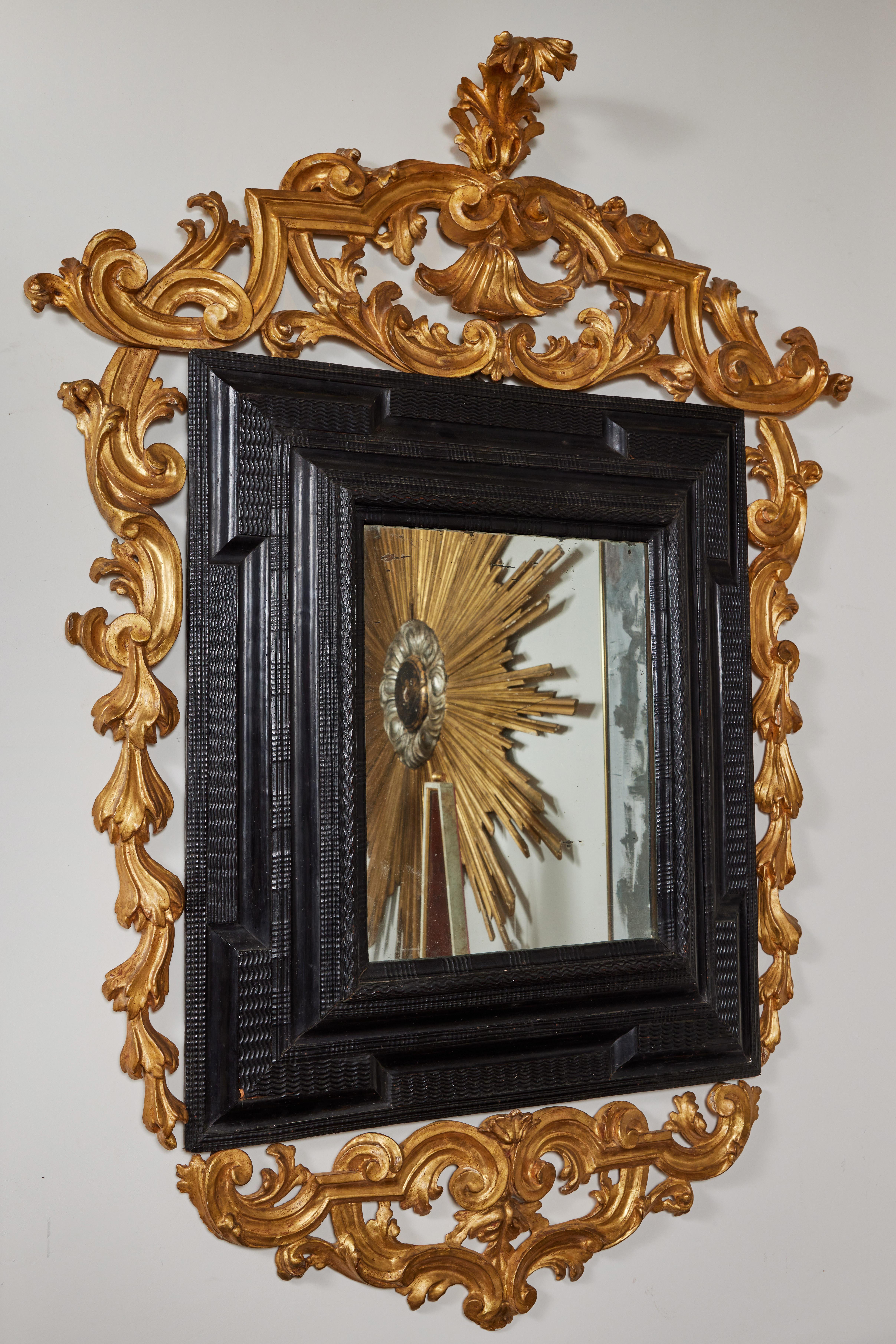 Remarquable miroir de style hollandais, sculpté à la main et ébénisé, orné de formes de vagues en relief. Le tout est entouré d'un cadre d'époque, en bois doré, percé de magnifiques volutes et terminé par une impressionnante couronne ornée d'une