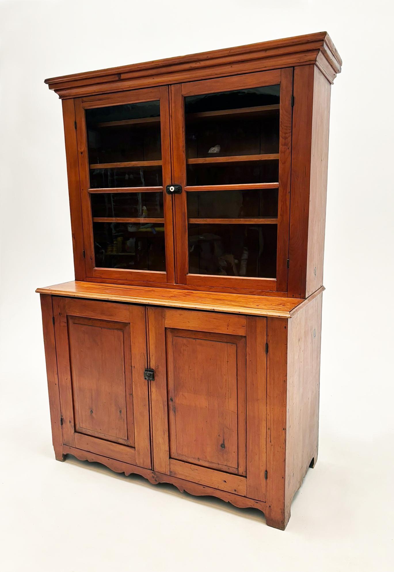 This simple, yet beautiful country pine cupboard features a primitive design of two solid doors on the bottom and two framed wavy glass doors on the top, which is set back allowing for a narrow counter area.

Beautiful American pine comprises this